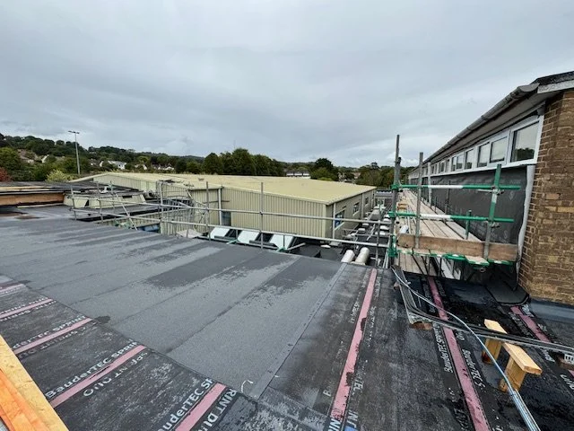 Rooftop under construction with scaffolding, roofing materials, and a cloudy sky.