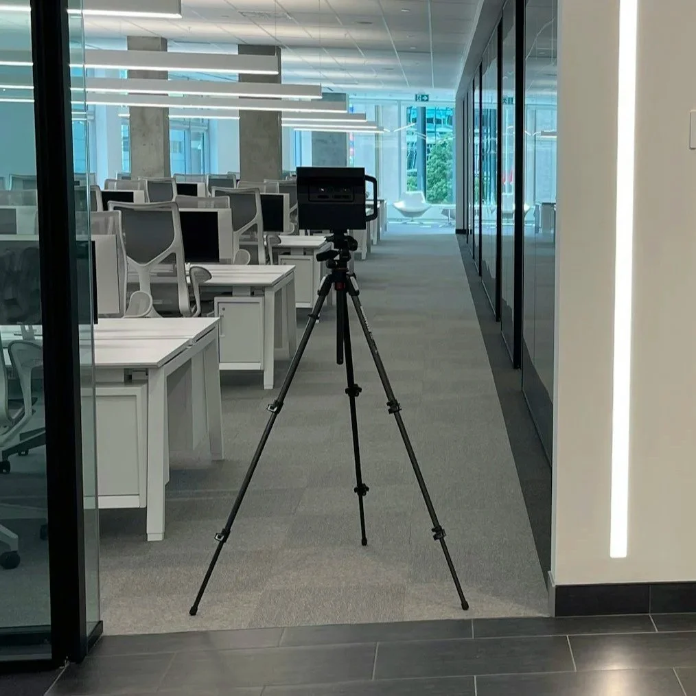 Empty modern office space with white desks, ergonomic chairs, and a camera on tripod facing the work area.