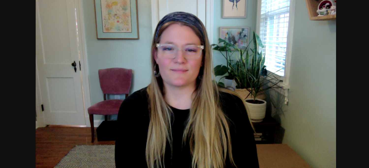 Headshot of Kristin Iacone sitting at her desk with pictures hanging on the wall and plants behind her.