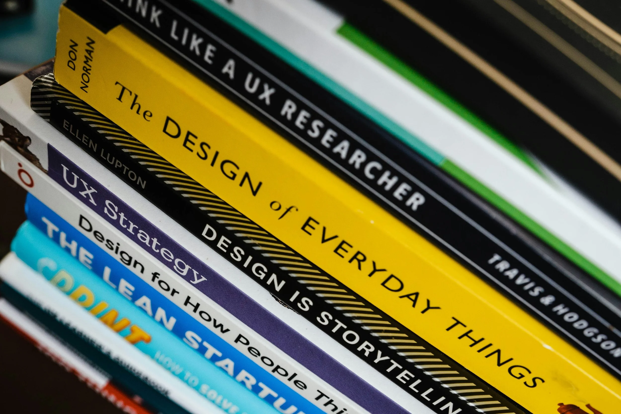 Stack of books on design, research, and storytelling with visible titles including "The Design of Every Day Things," "Design is Storytelling," and "Storytelling."