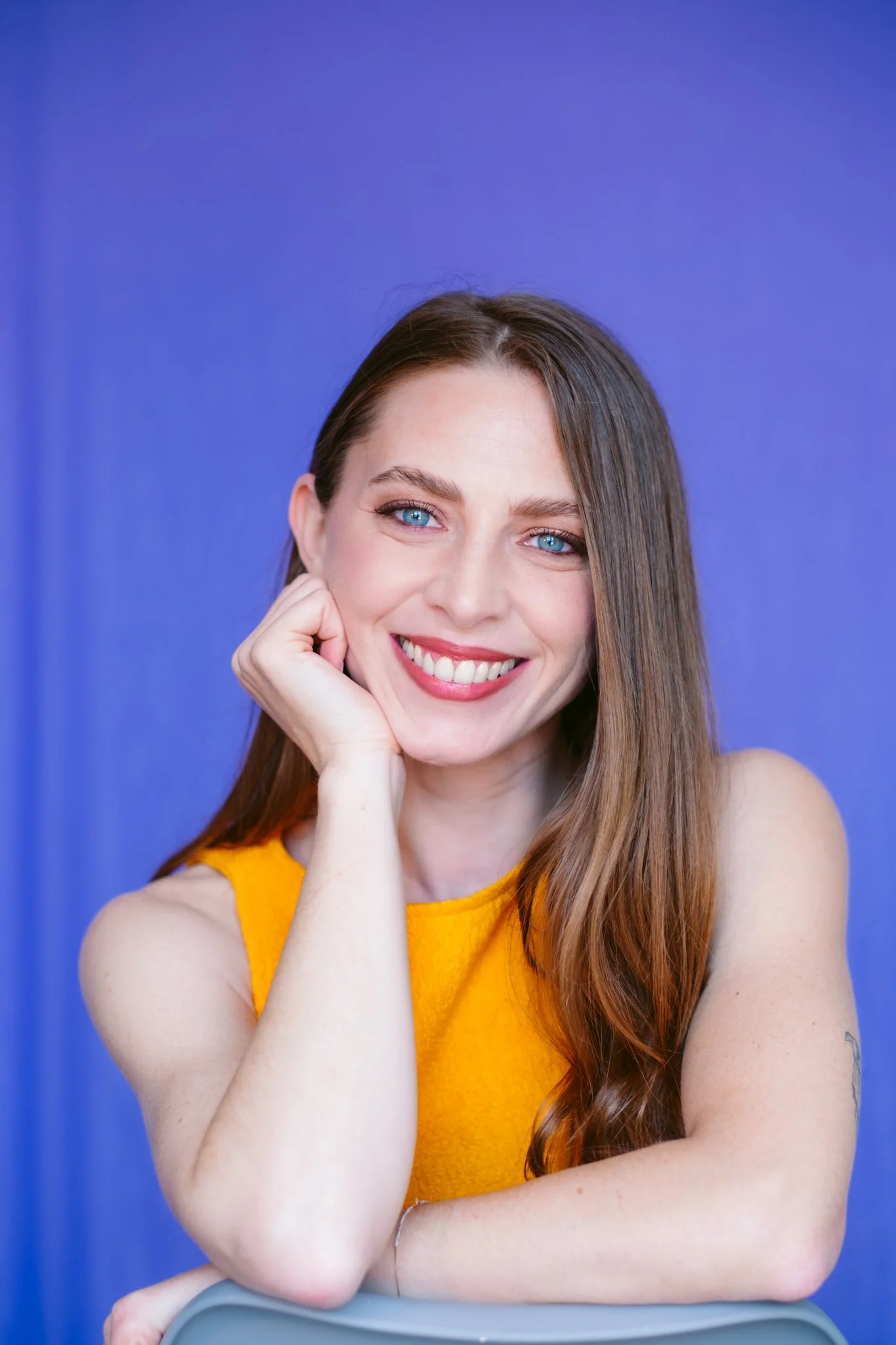 Ragazza con capelli marroni, occhi azzurri e sorriso, indossa top giallo, sfondo blu