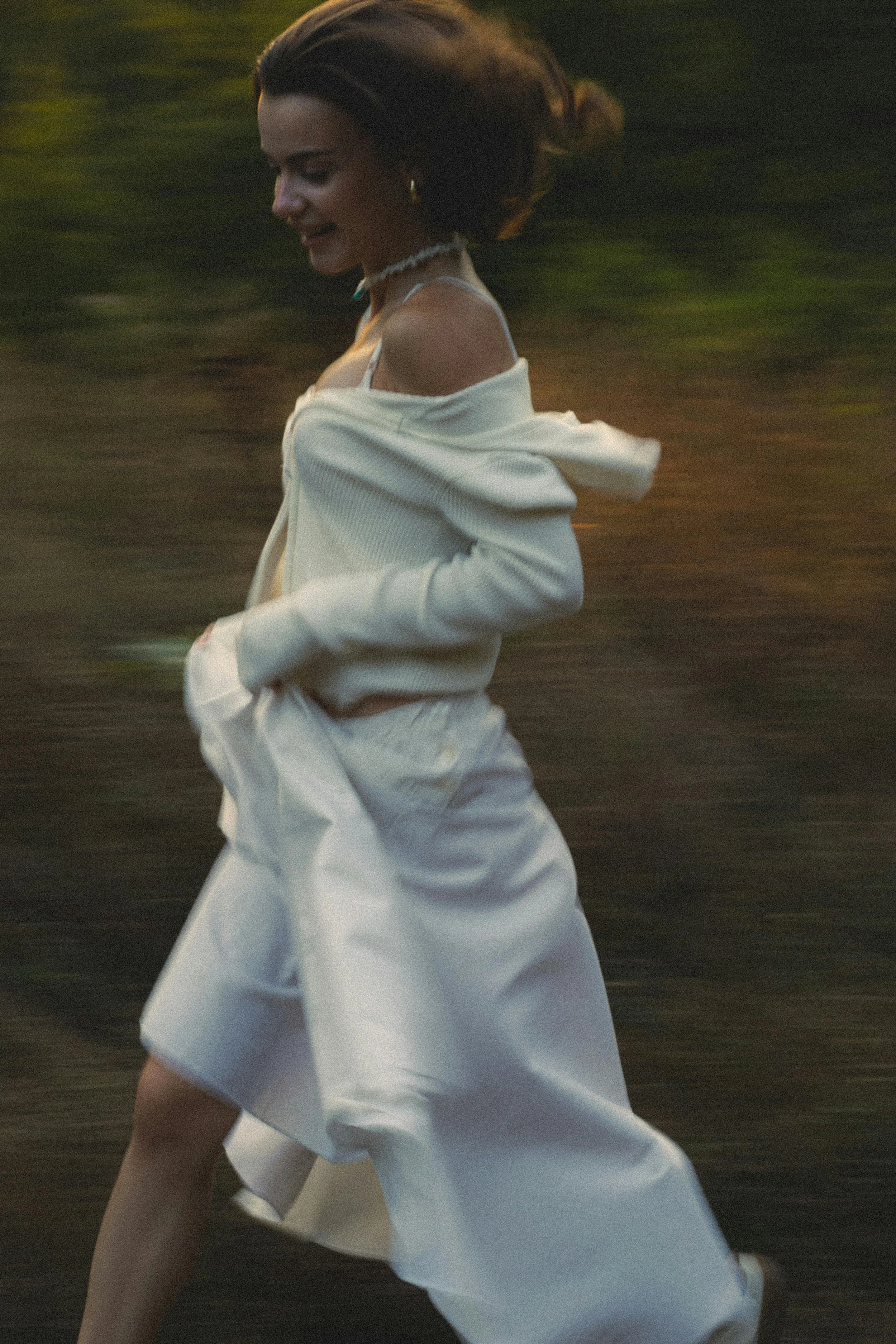 A woman with dark hair wearing a white outfit, running outdoors, possibly at sunset or dawn.