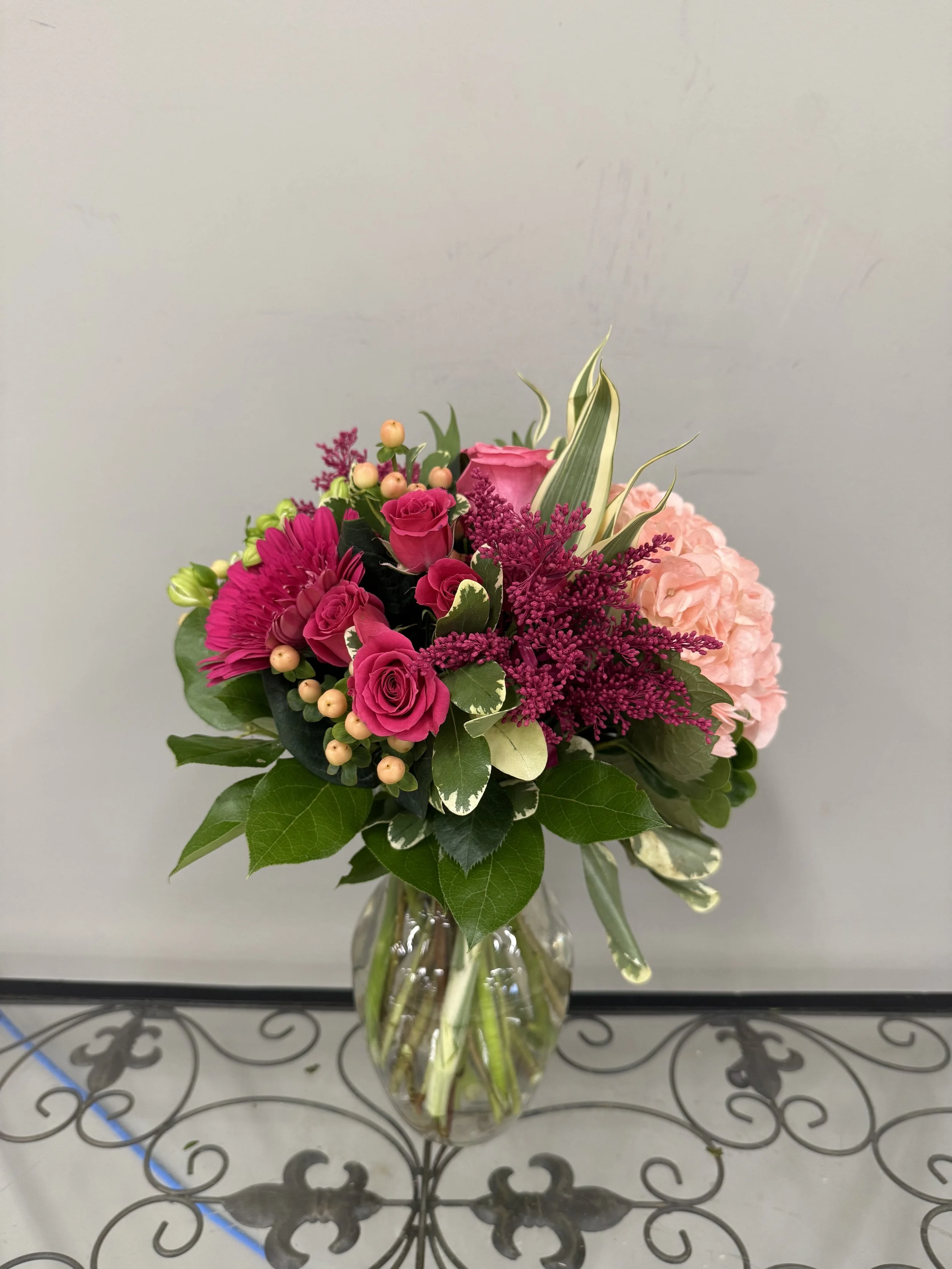 A colorful bouquet of pink and purple flowers in a clear glass vase on a decorative metal table.