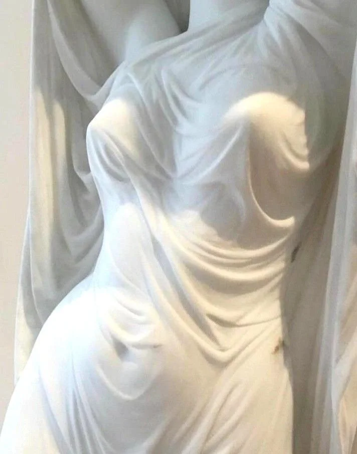 Close-up of a classical white marble sculpture of a woman with draped clothing.