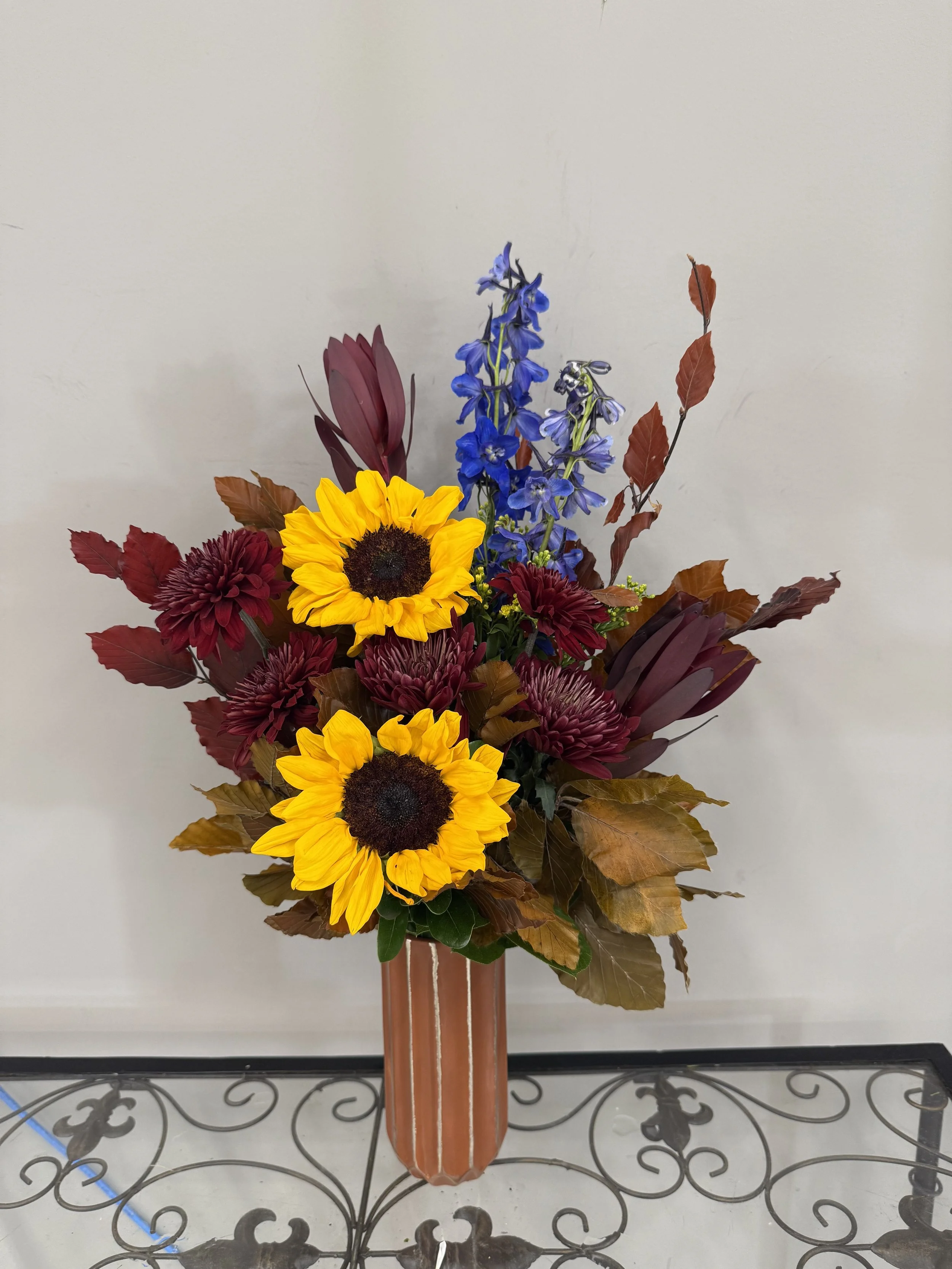 A bouquet of colorful flowers in a brown striped vase, placed on a glass table with decorative metalwork.