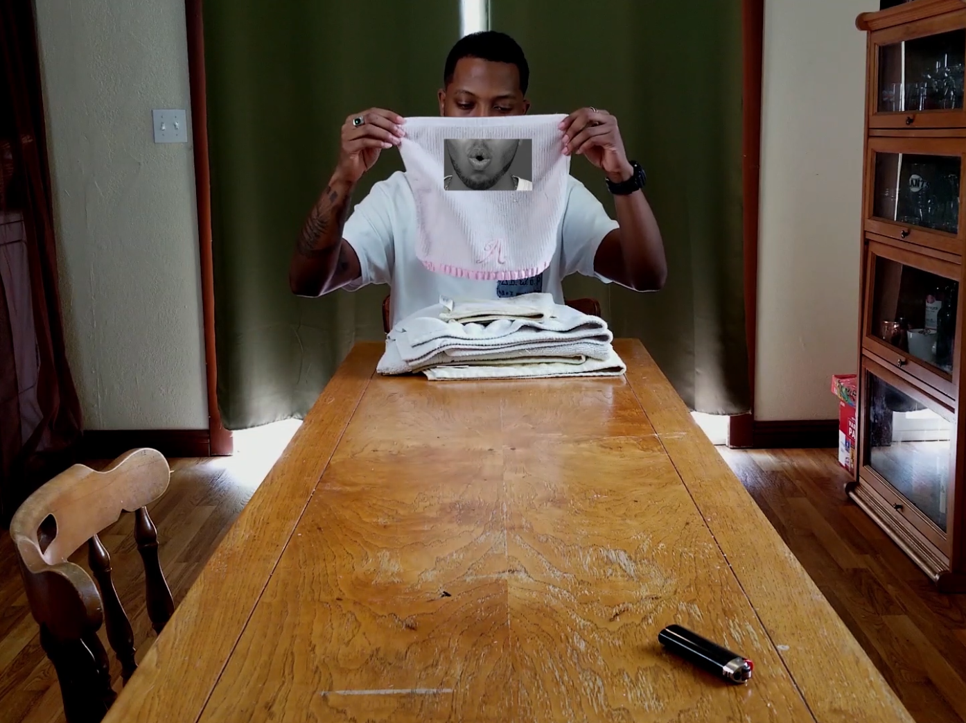 A man sitting at the end of a table with a rag in front of his face. 
