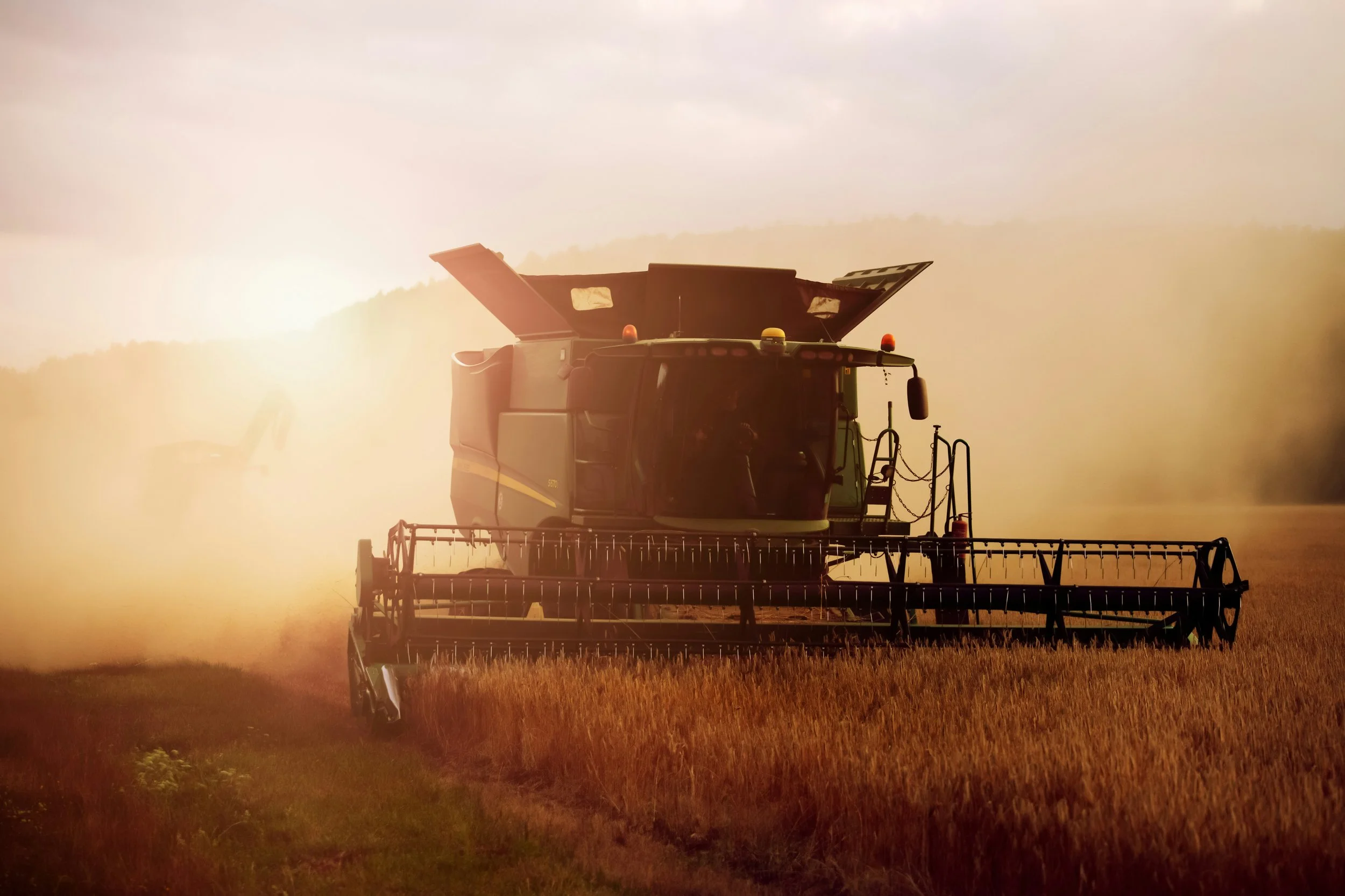 A combine harvester working in a wheat field during a dusty golden sunset, capturing the motion and intensity of harvest season.