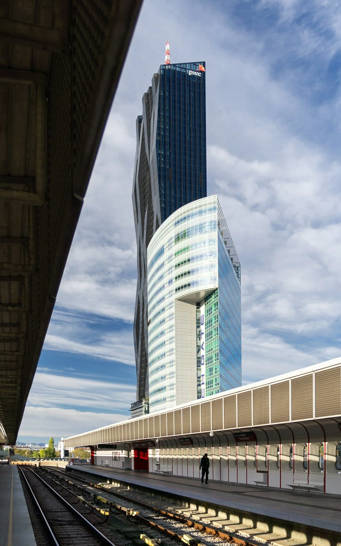 Vienna landmark: DC Tower 1 and Tech Gate Vienna showcasing their unique, geometric forms, prominent glass facades, and a train station platform. Modern architecture in Austria.