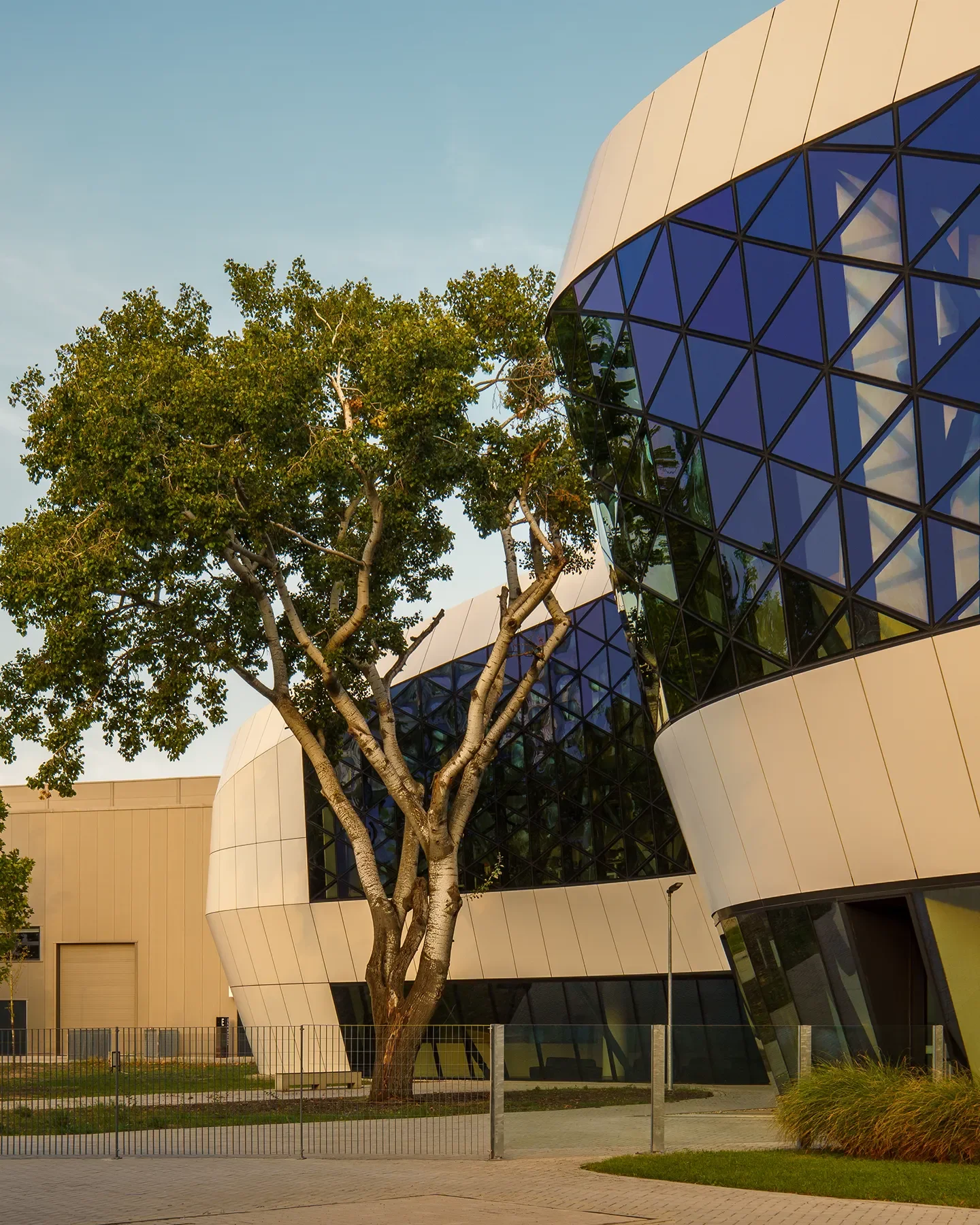 Hungexpo F1 Reception Building in Budapest showing curved triskelion-shaped architecture, front and rear visible with large tree in center