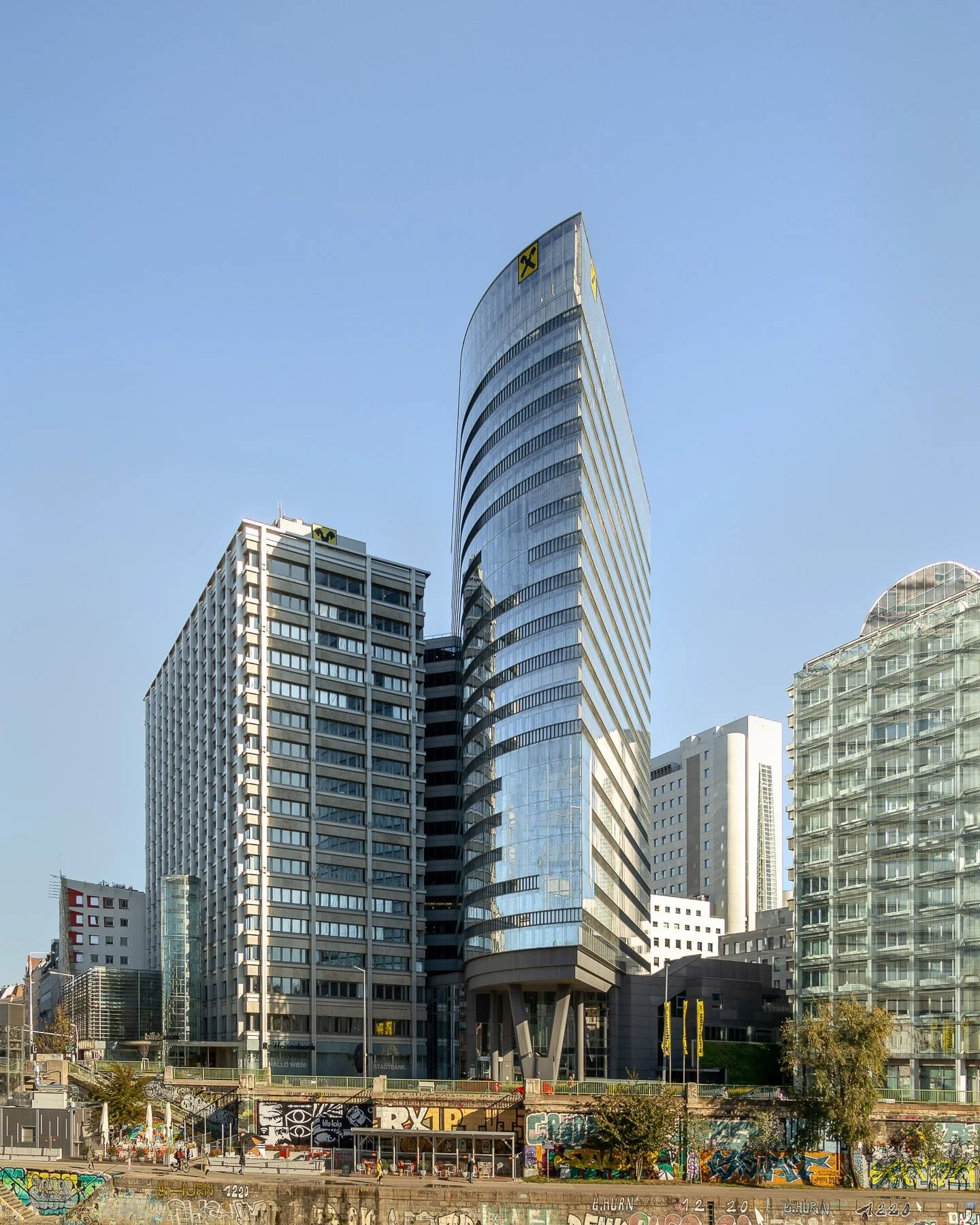Modern architecture in Vienna: Raiffeisen Tower featuring its distinctive shape, reflective glass surfaces, and a prominent location along the Danube Canal with graffiti art adding an urban touch.