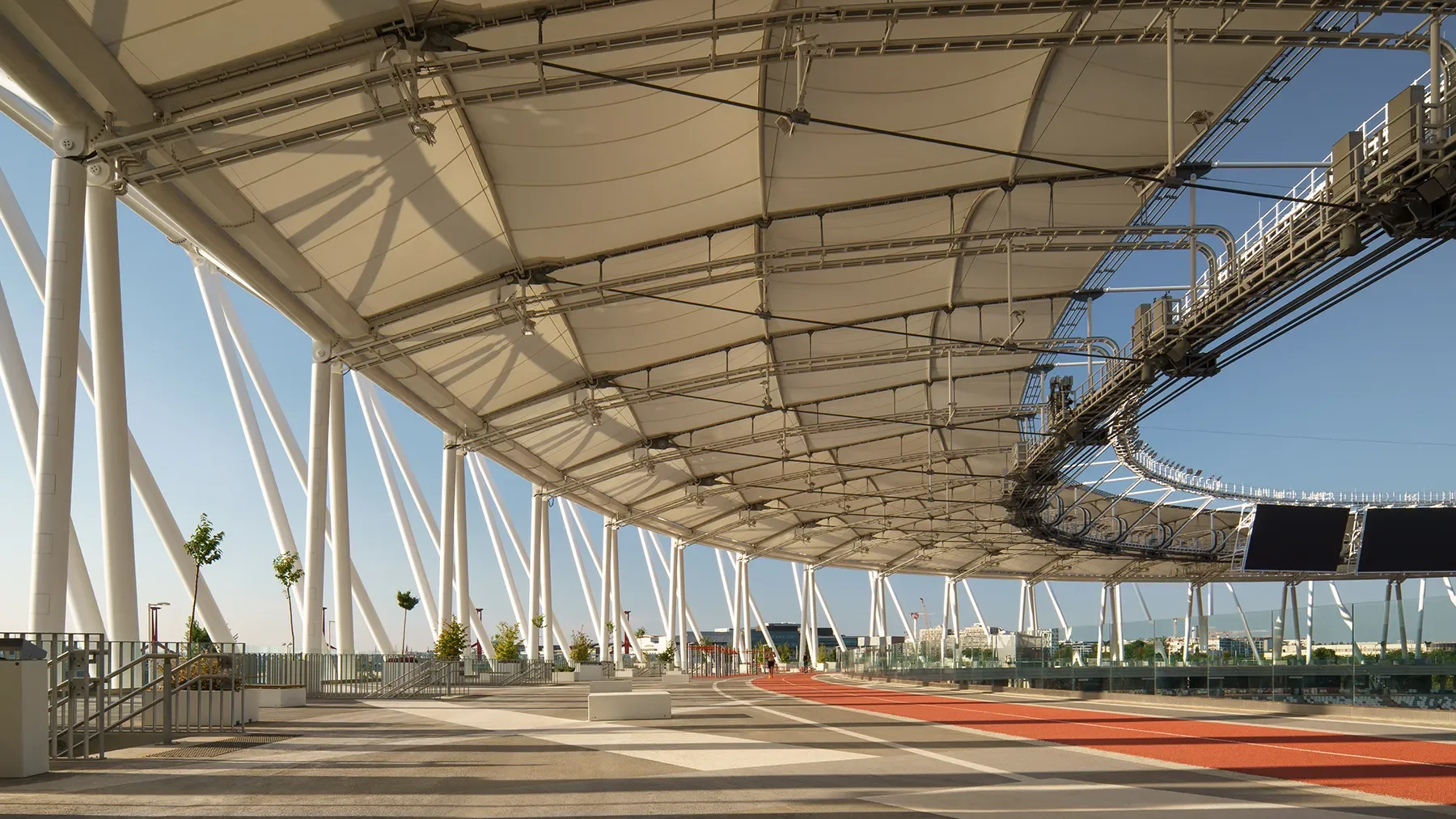 Wide first-level view of Budapest Athletics Stadium public track with roof structure, sunset light, and greenery