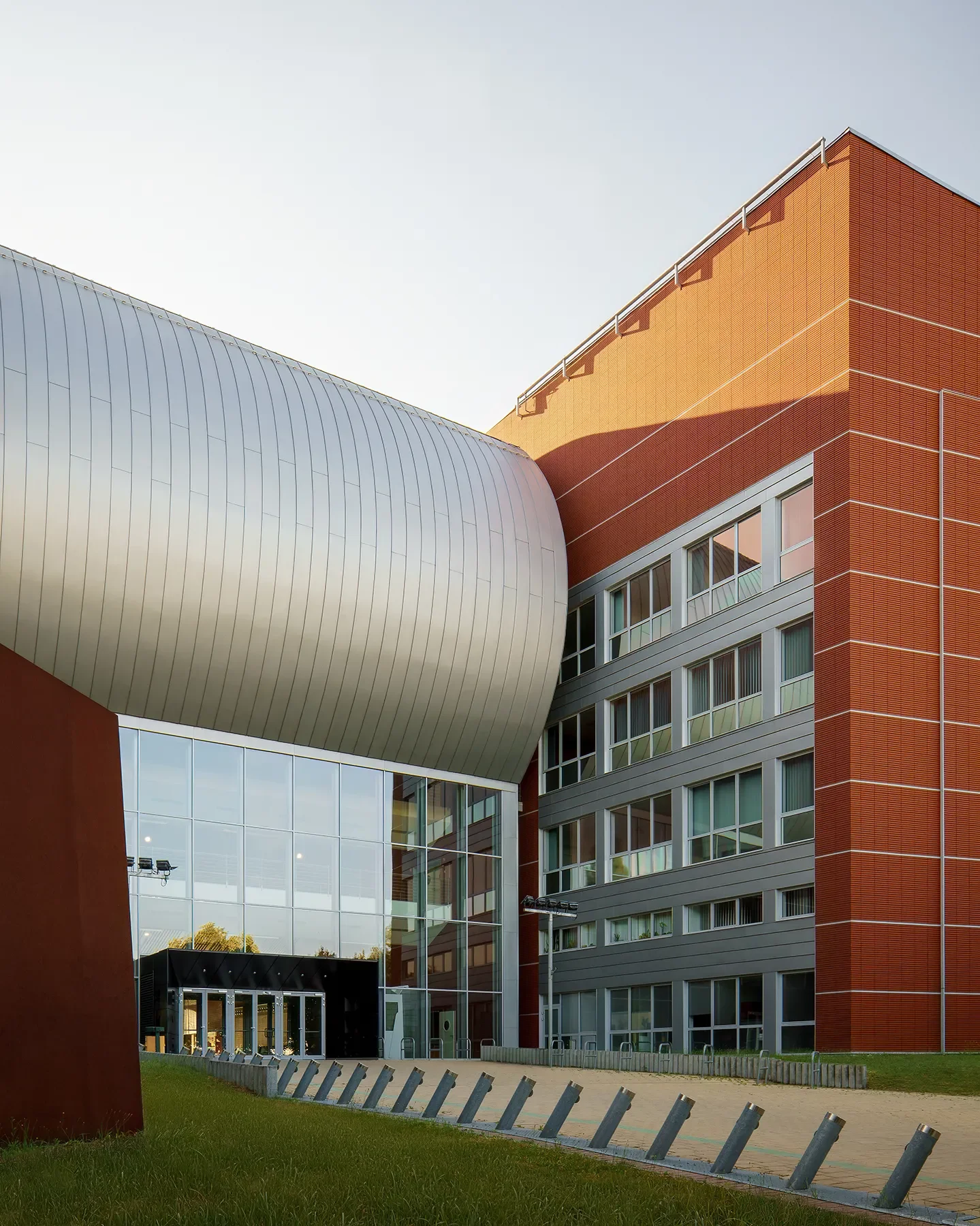 Main entrance of BME Q Building at Infopark Budapest in morning shadow, large windows and metal roof visible