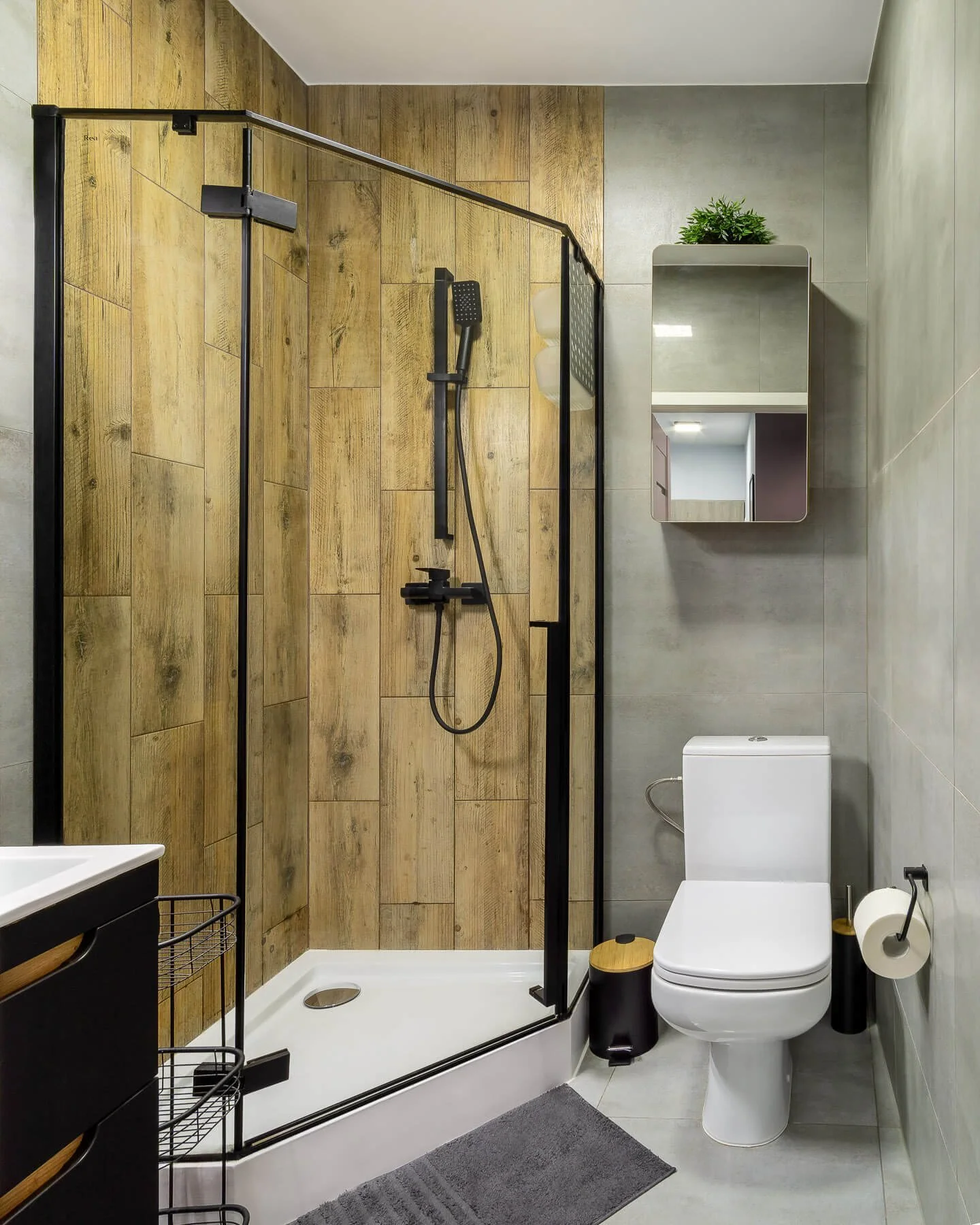 Modern bathroom design: Features a black framed glass shower enclosure, wood-look tile accent wall, and gray tile.