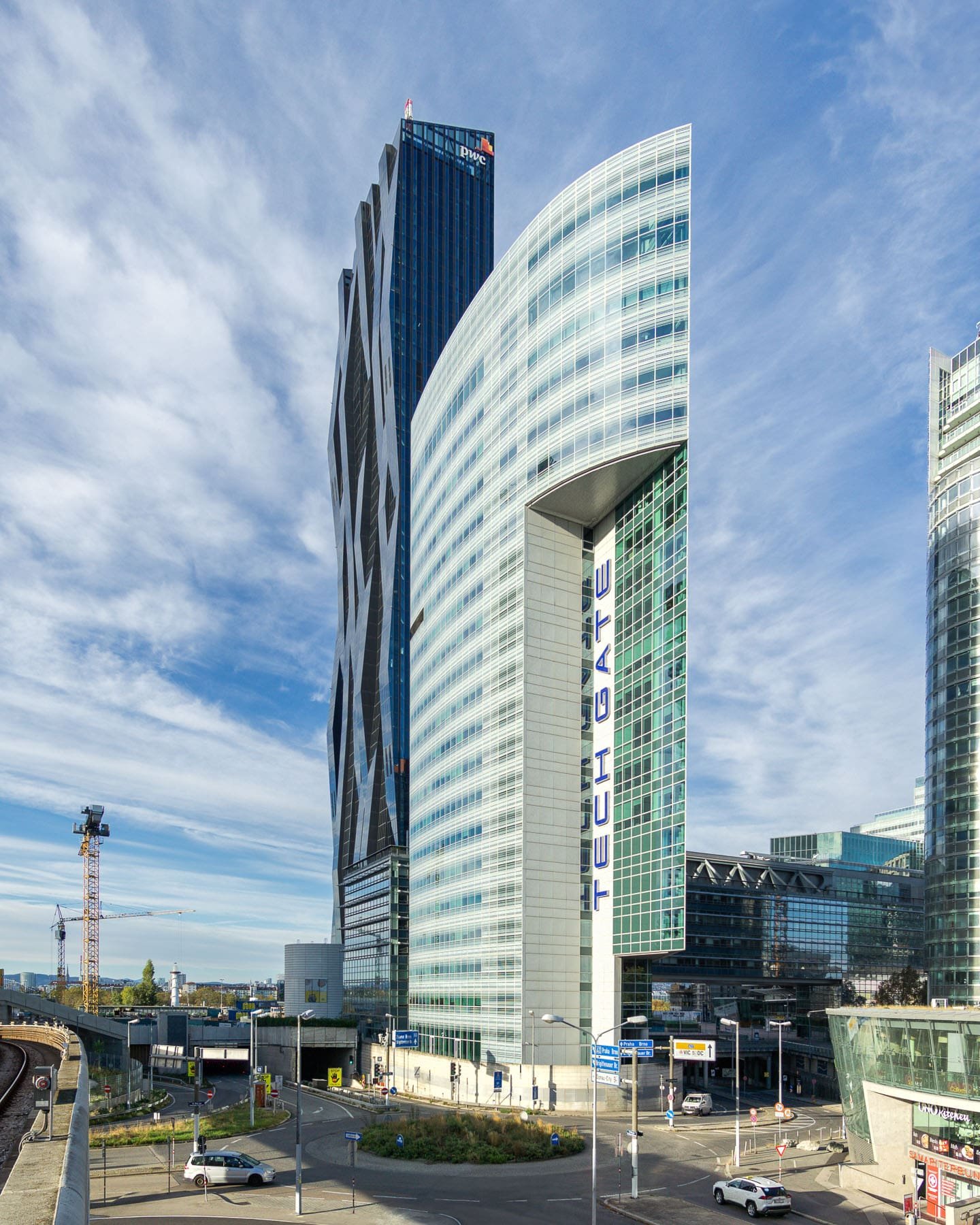 Vienna landmark: DC Tower 1 and Tech Gate Vienna showcasing their unique, geometric forms, prominent glass facades, and the "TECH GATE" signage. Modern architecture in Austria, with a crane and roadways visible.
