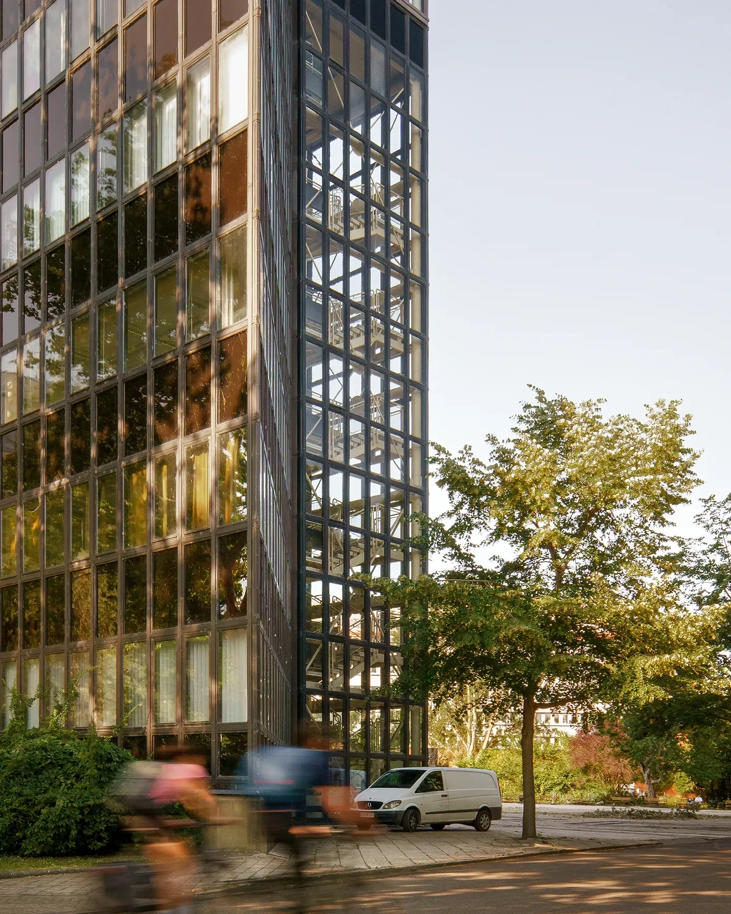 Side view of ELTE glass facade at Infopark Budapest with 2 blurry cyclists in foreground, dynamic perspective