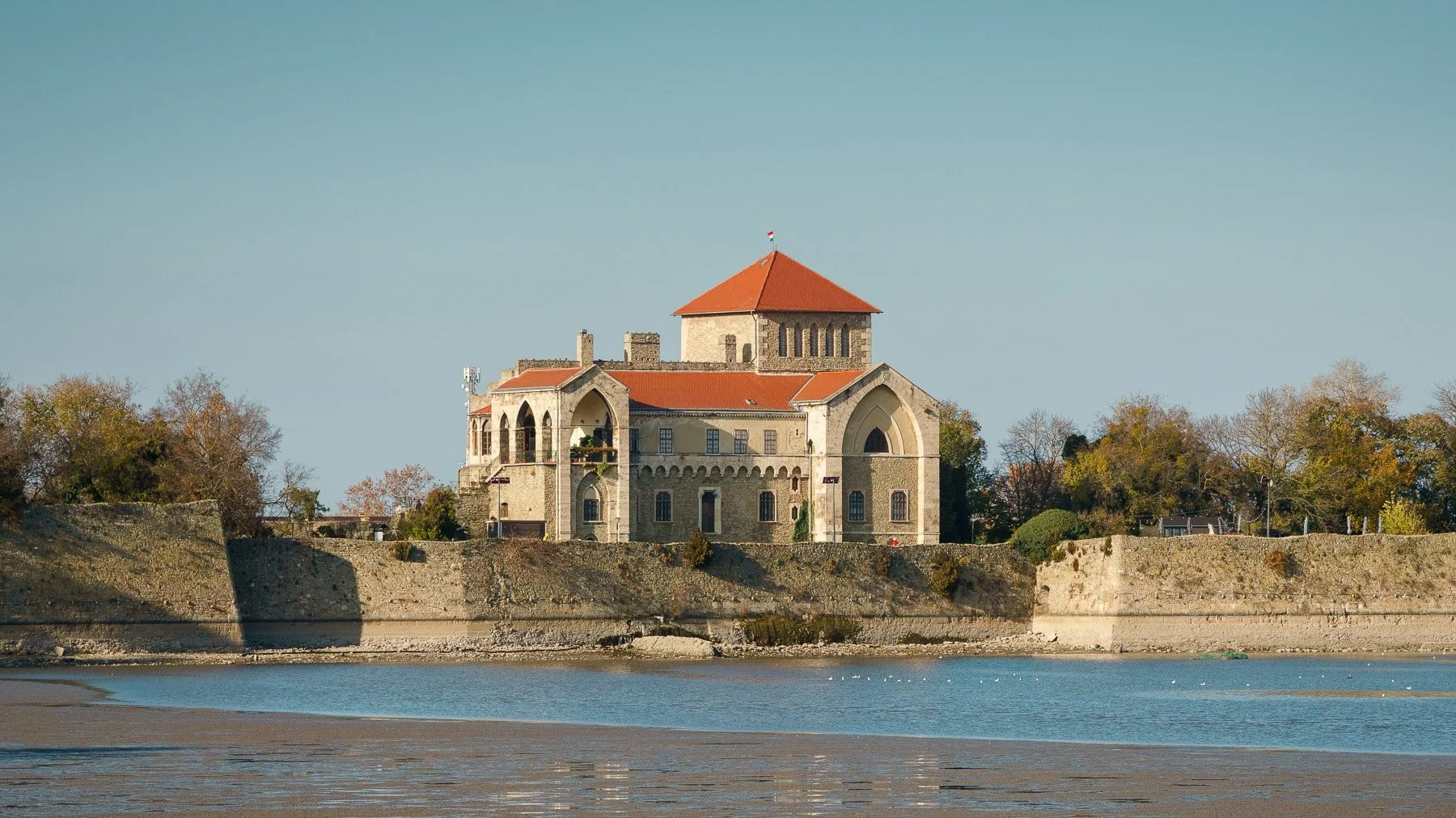 Tata, Hungary: Tata Castle, a historic fortress with a prominent red roof and stone ramparts, reflected in the calm waters of the lake