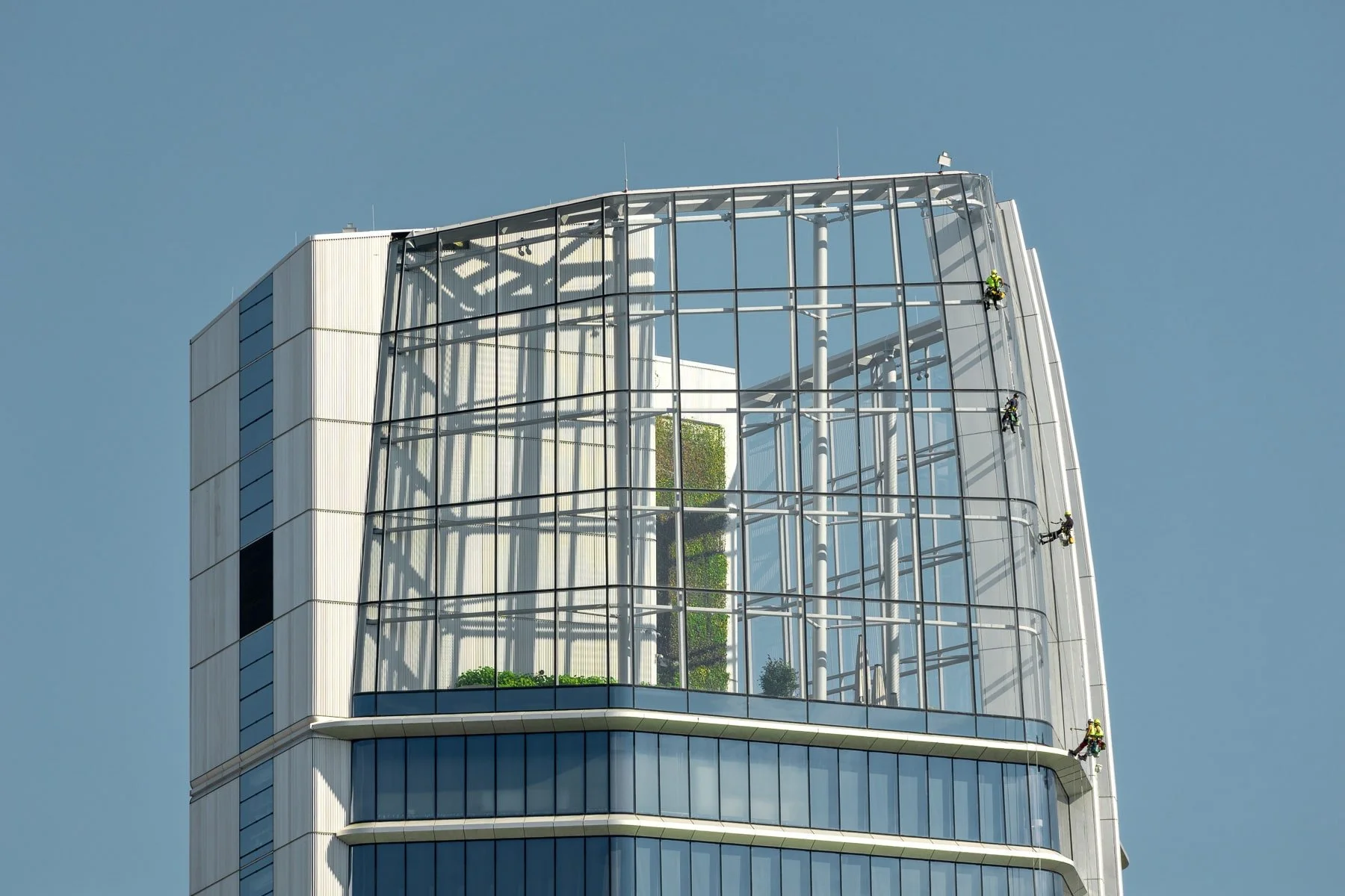 Budapest, Hungary: MOL Campus building featuring a modern glass facade and visible structural elements, with window cleaners visible on the upper levels. Close-up view emphasizing the building's architectural details.