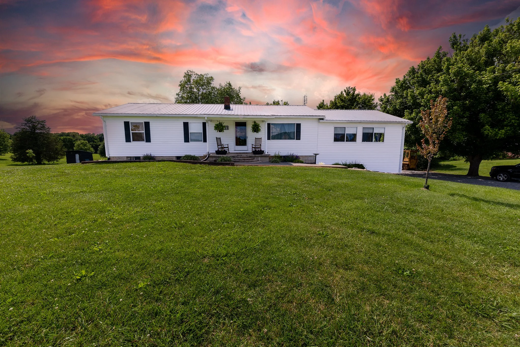 White house with black shutters on a grassy lawn during sunset with pink and orange clouds in the sky