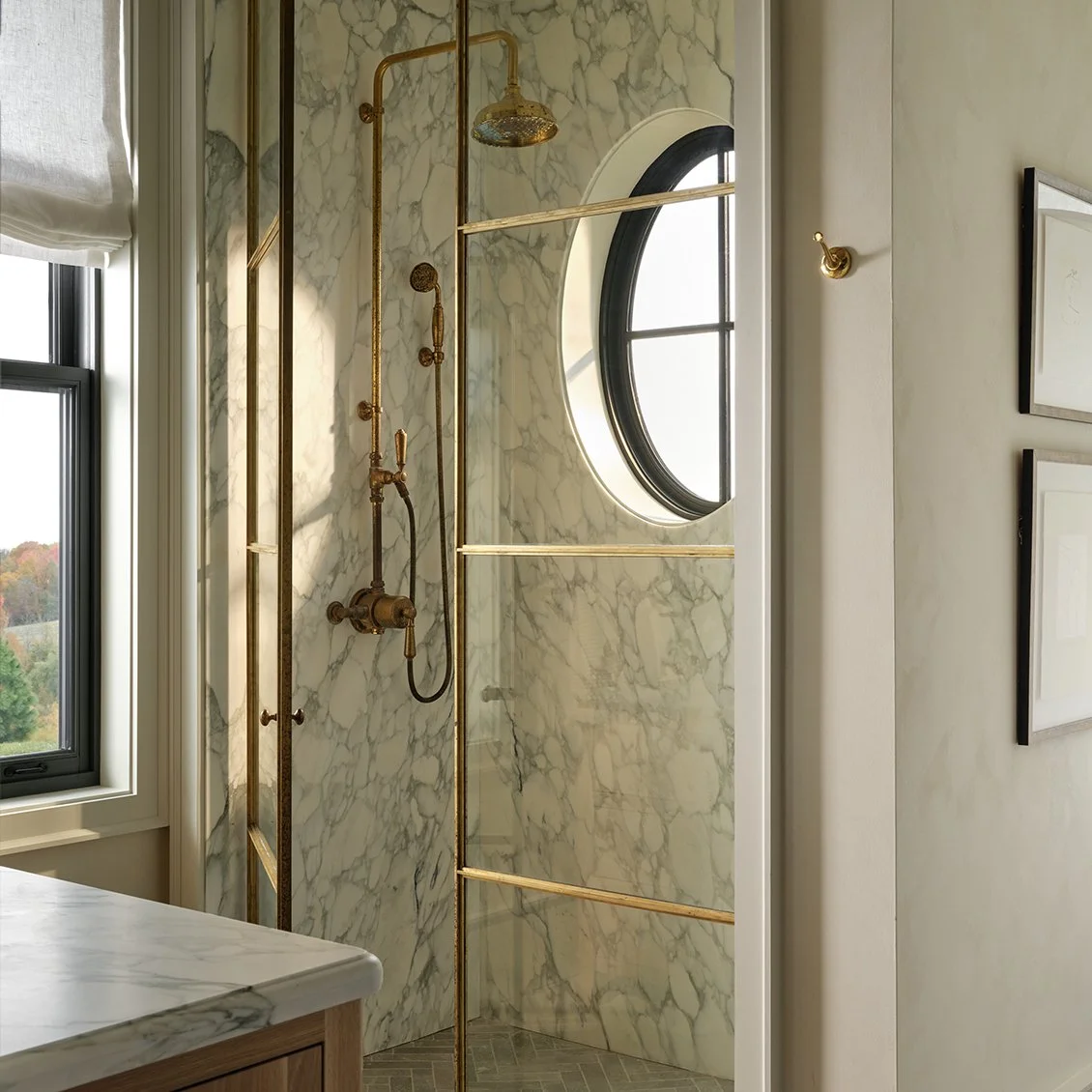Luxurious bathroom with brass shower fixtures, marble walls, and a round window.