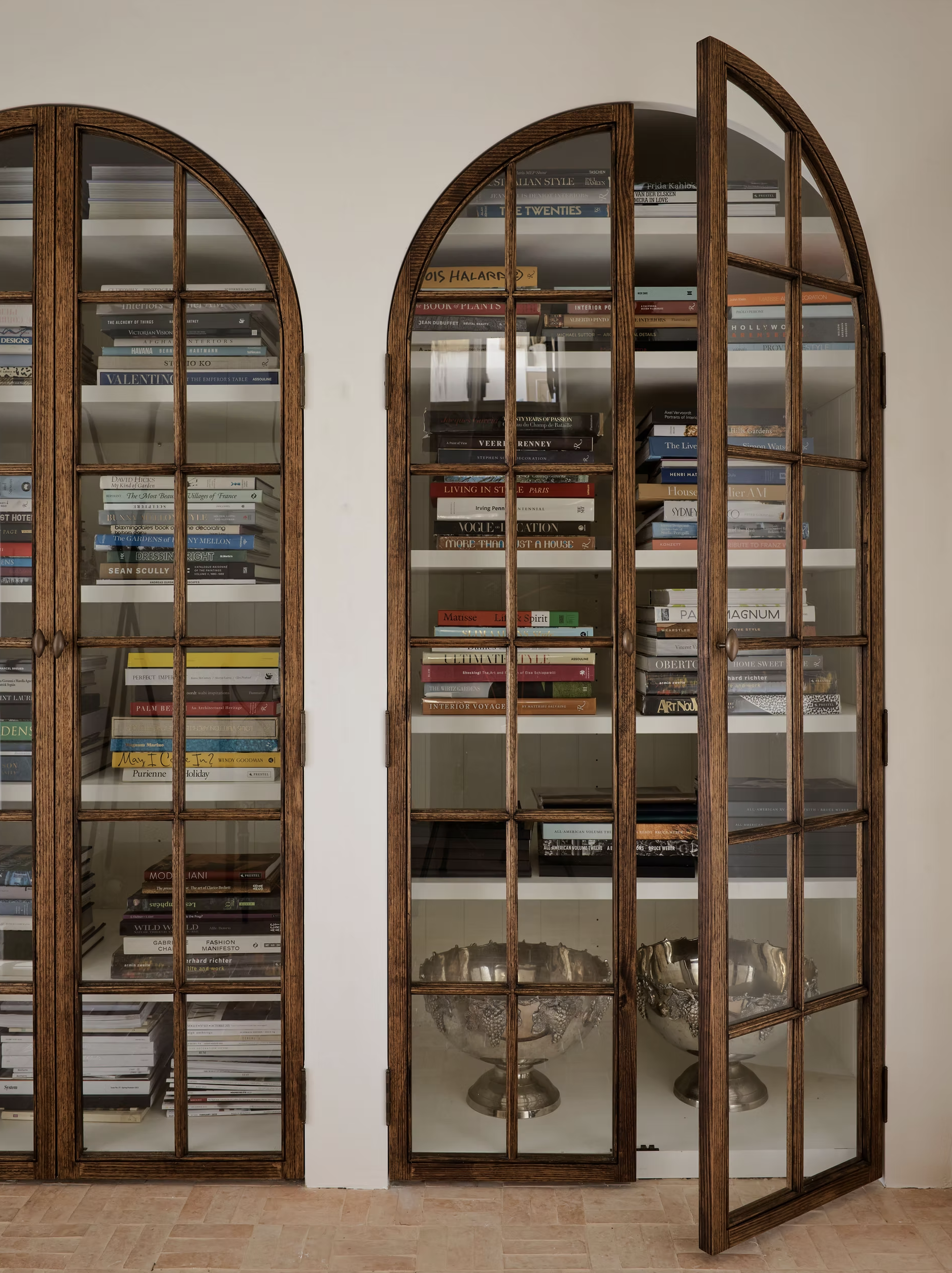 Bookshelves with arched glass doors filled with books and silver bowls.
