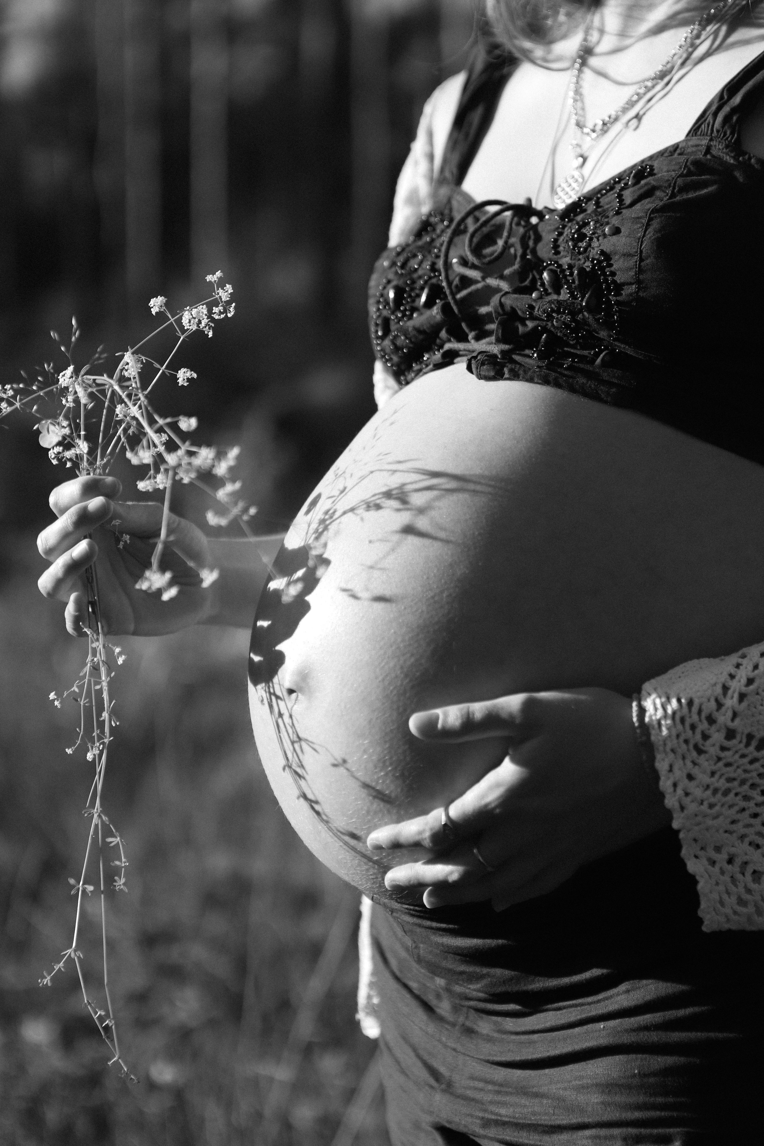 embodied portrait of a woman by Alice Rose Photography in natural light..Black and white photo of a pregnant woman holding flowers next to her belly.