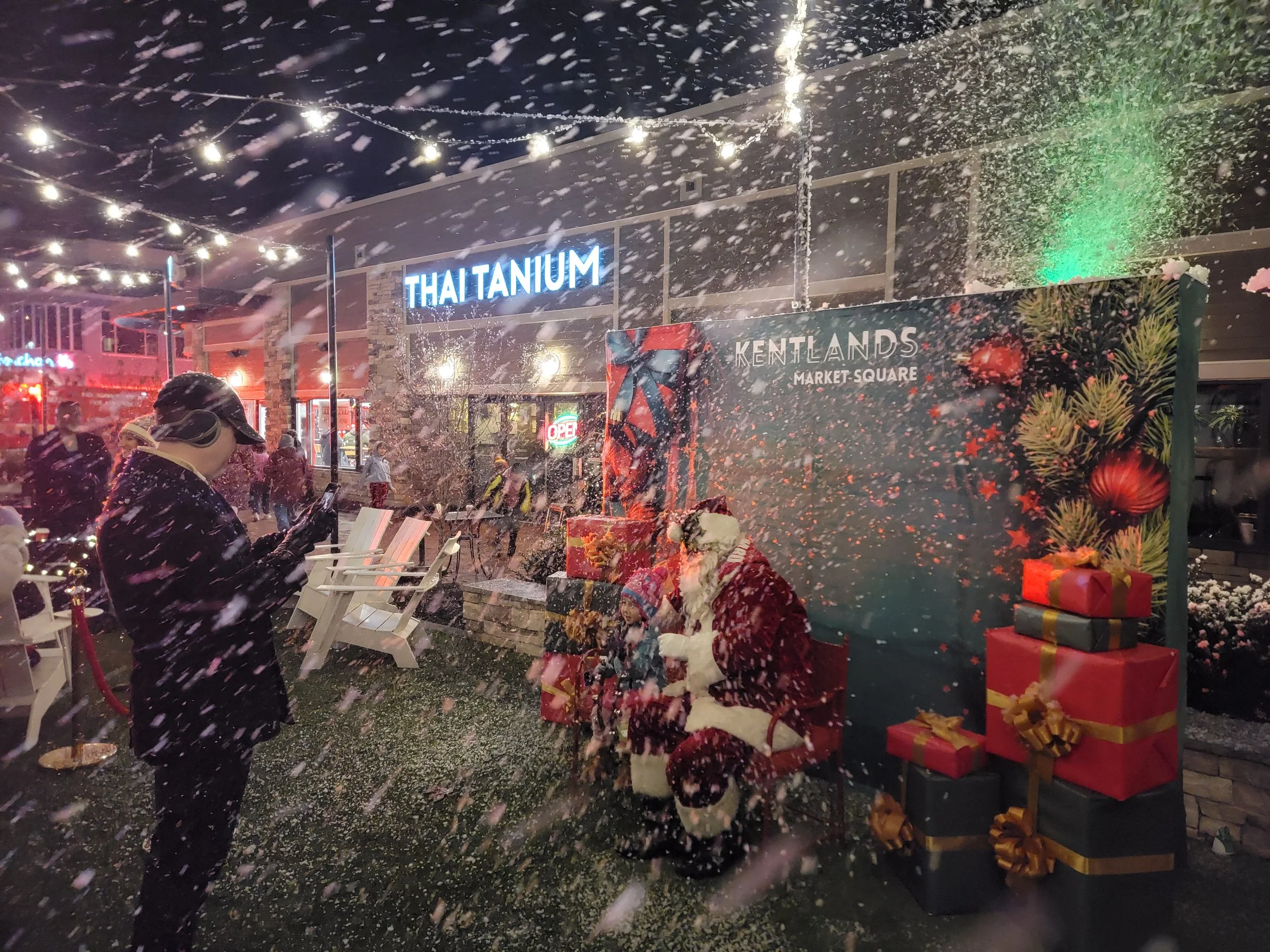 Santa surrounded by presents with artificial snow at the Tree and Menorah Lighting event