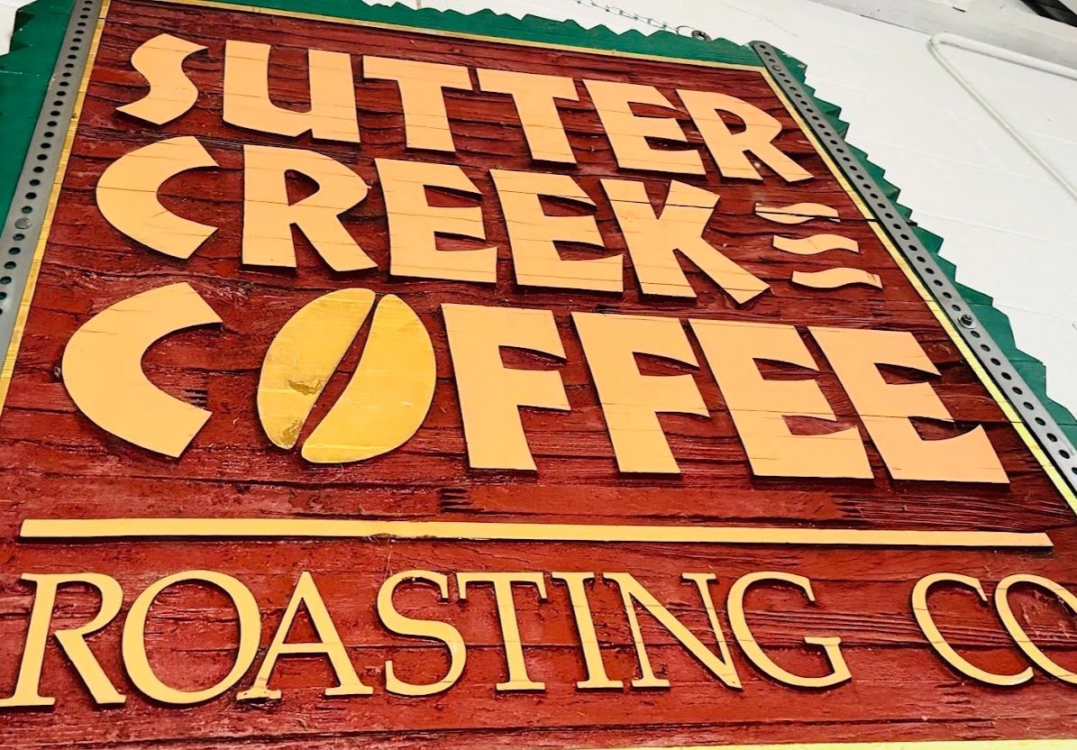 Wooden sign for Suttrer Creek Coffee with roasted coffee beans graphic and the words "Roasting Co." below.