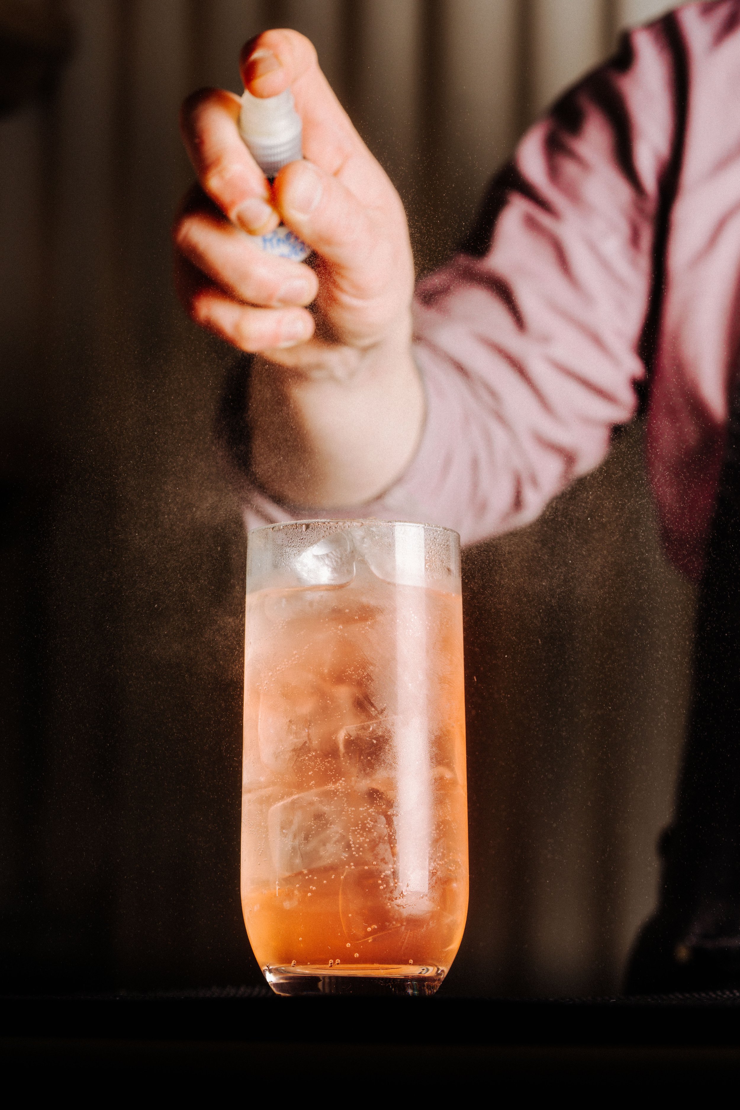 Fallachan Dining - Bartender spraying a garnish over a cocktail in a tall glass with ice, creating a mist effect.