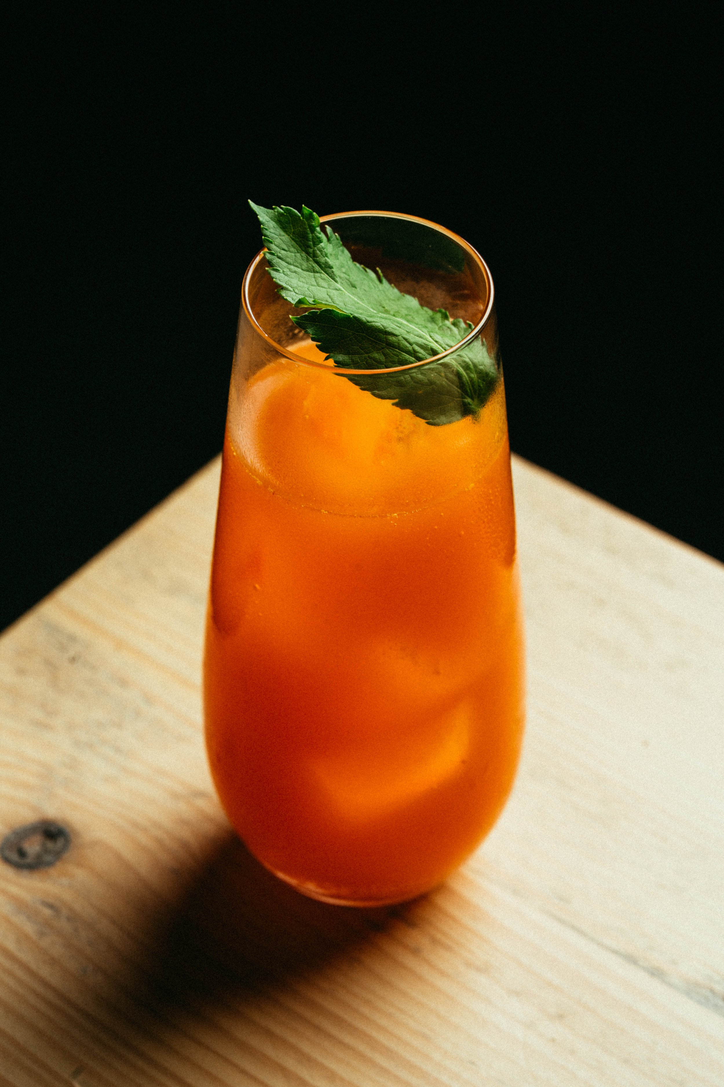 Fallachan Dining - Orange drink in a glass with mint garnish on wooden surface.