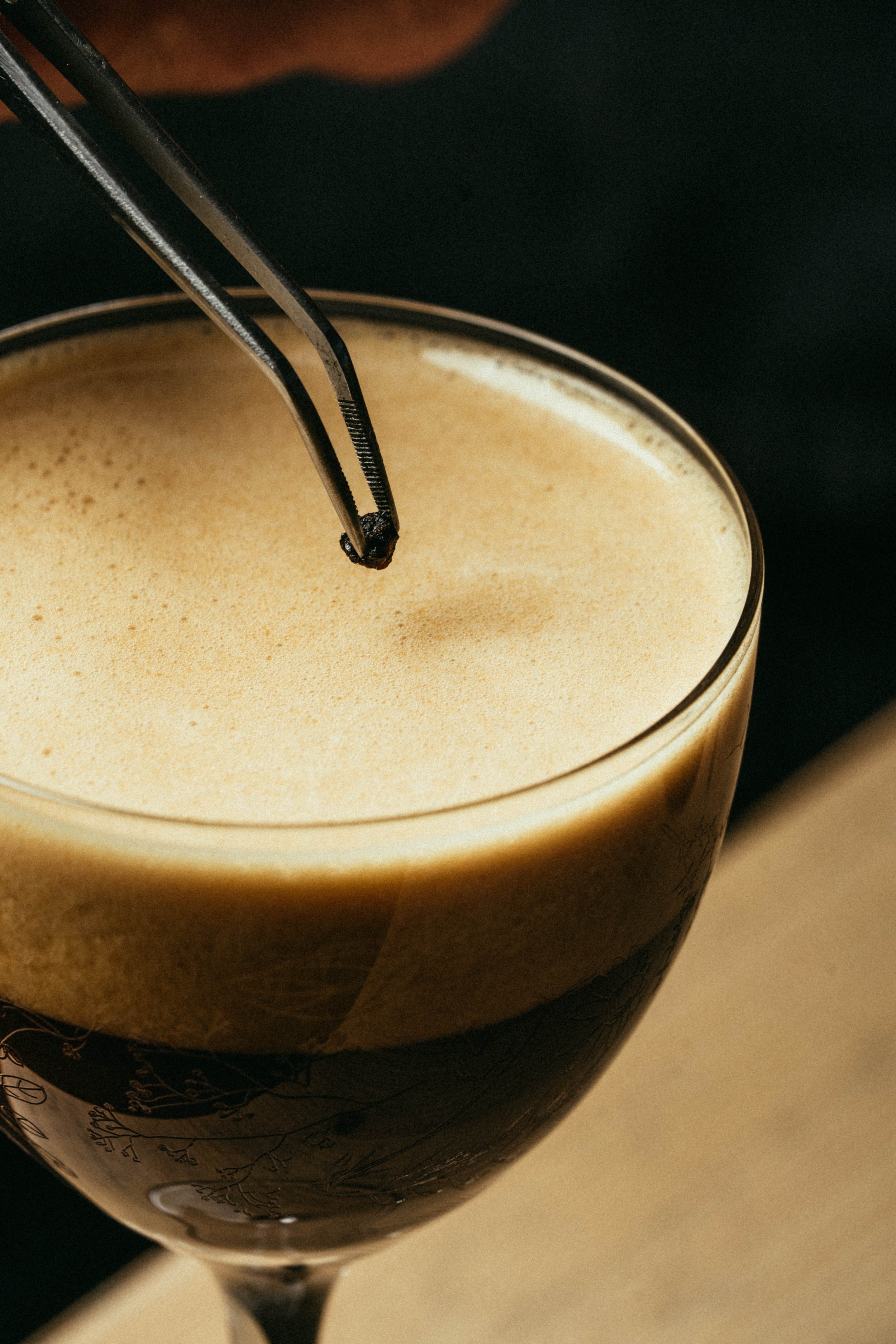 Fallachan Dining - Close-up of a dark espresso martini garnished with a coffee bean using tweezers.