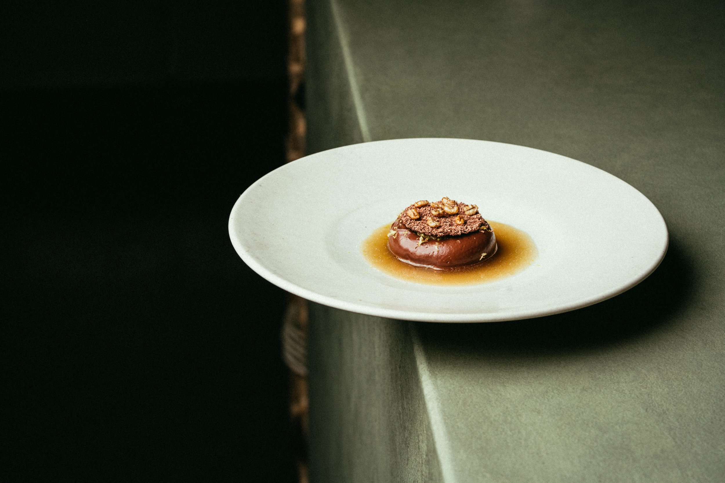 Fallachan Dining - Gourmet dish with a small portion of food on a minimalist white plate, placed on a green textured surface.