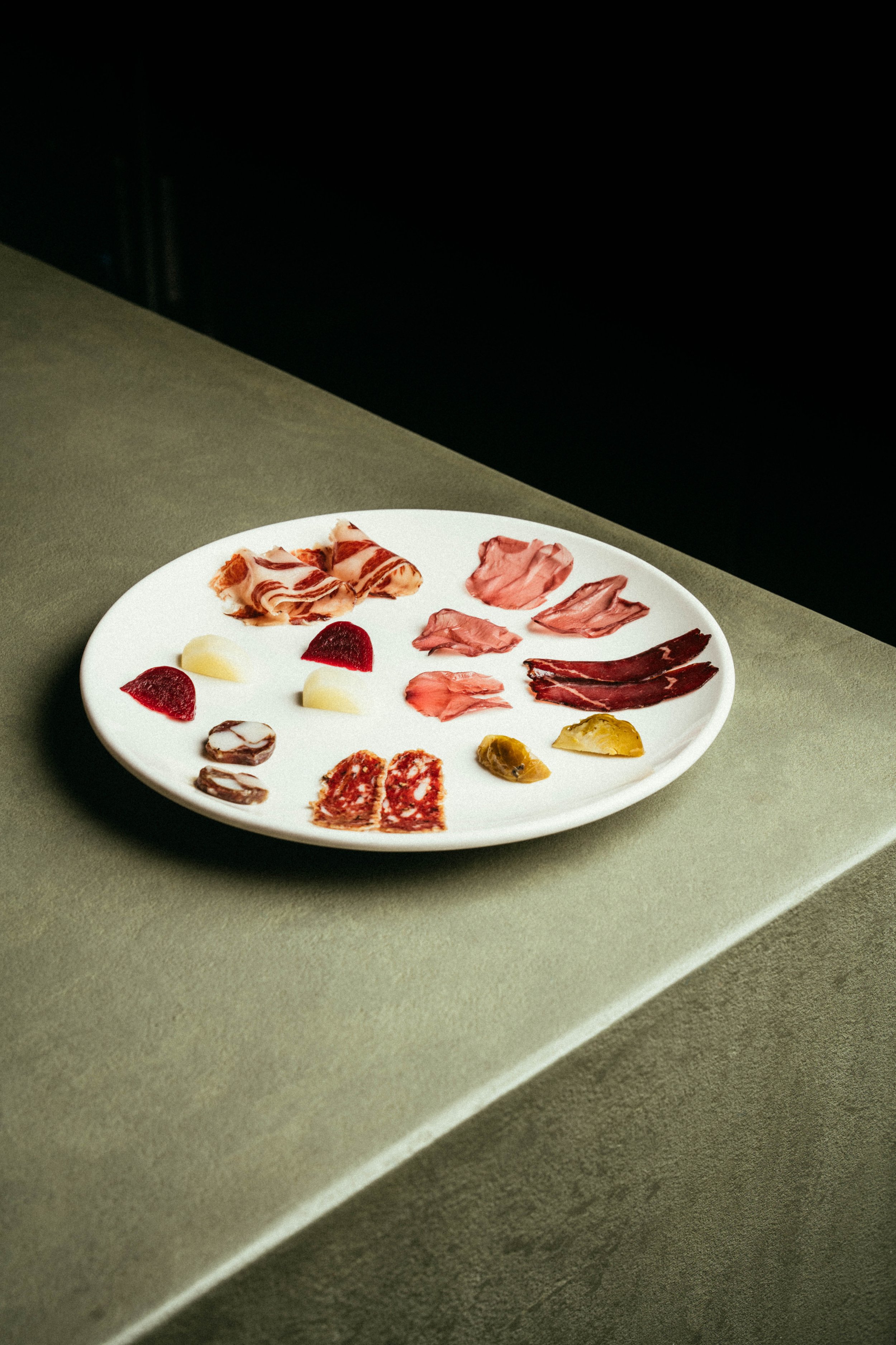 Fallachan Dining - White plate with assorted cured meats and cheeses on a concrete surface.
