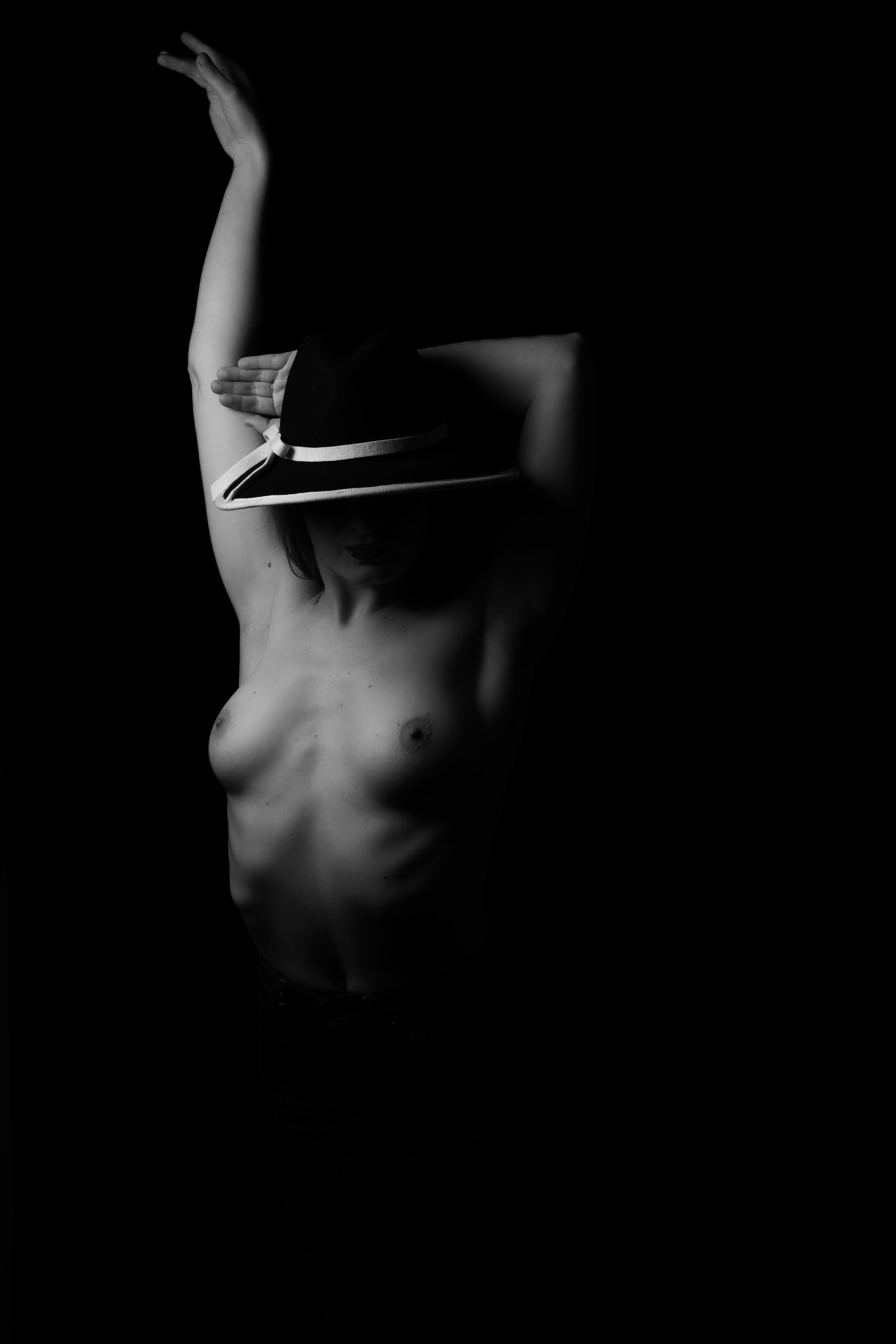 Une personne topless portant un chapeau, posant dans un style artistique en noir et blanc.