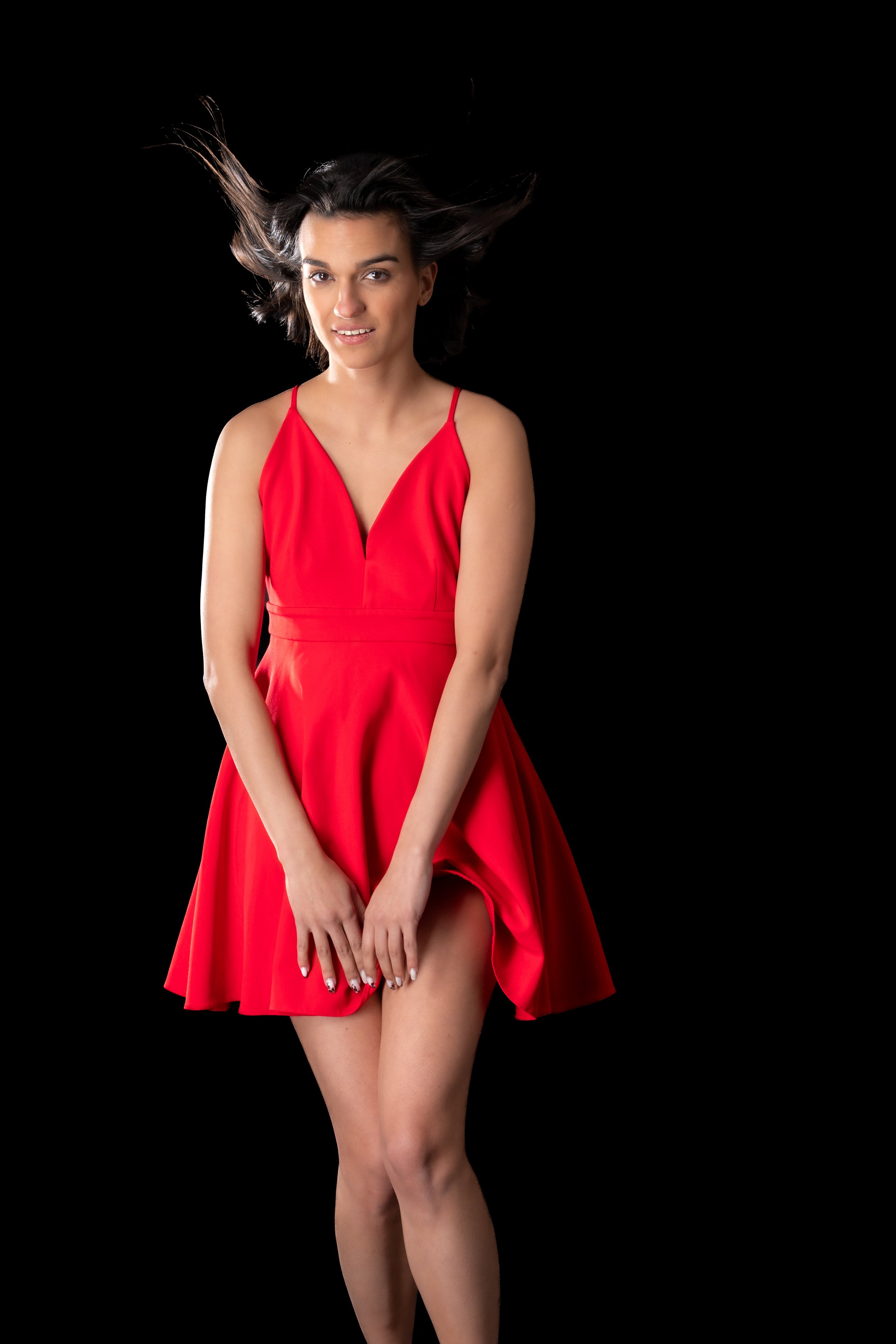 Femme en robe rouge sur fond noir, cheveux flottants.