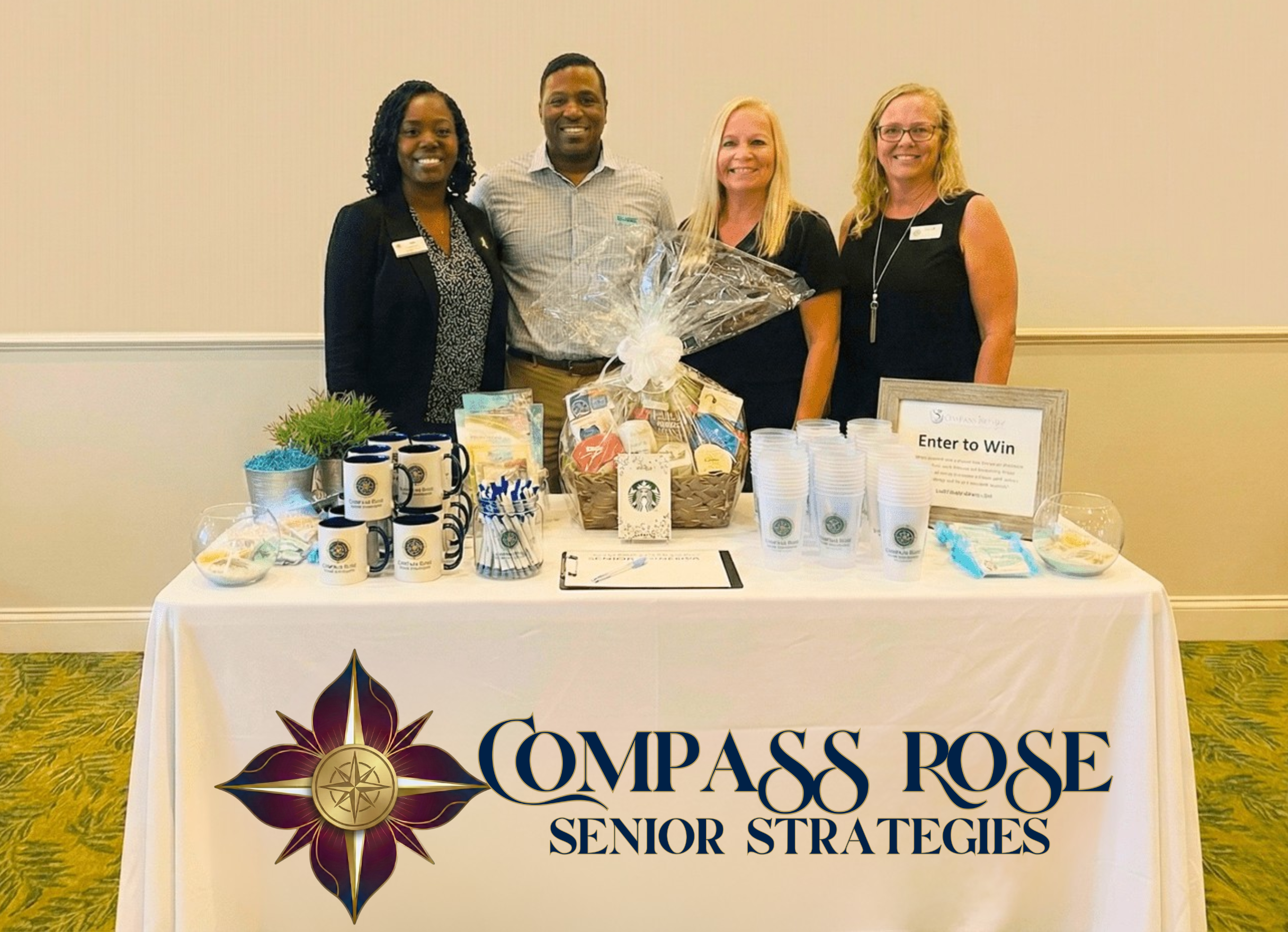 Four women and one man standing behind a table with promotional items and a large gift basket. The table has a banner that reads "Compass Rose Senior Strategies" and a logo. The table includes Starbucks cups, pens, brochures, and a sign that says "Enter to Win." The setting appears to be an indoor event or conference.