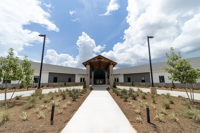 Front view of a modern, single-story building with a central entrance, set against a partly cloudy sky.