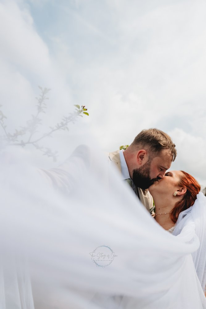 Wedding couple sharing a kiss by the brides veil