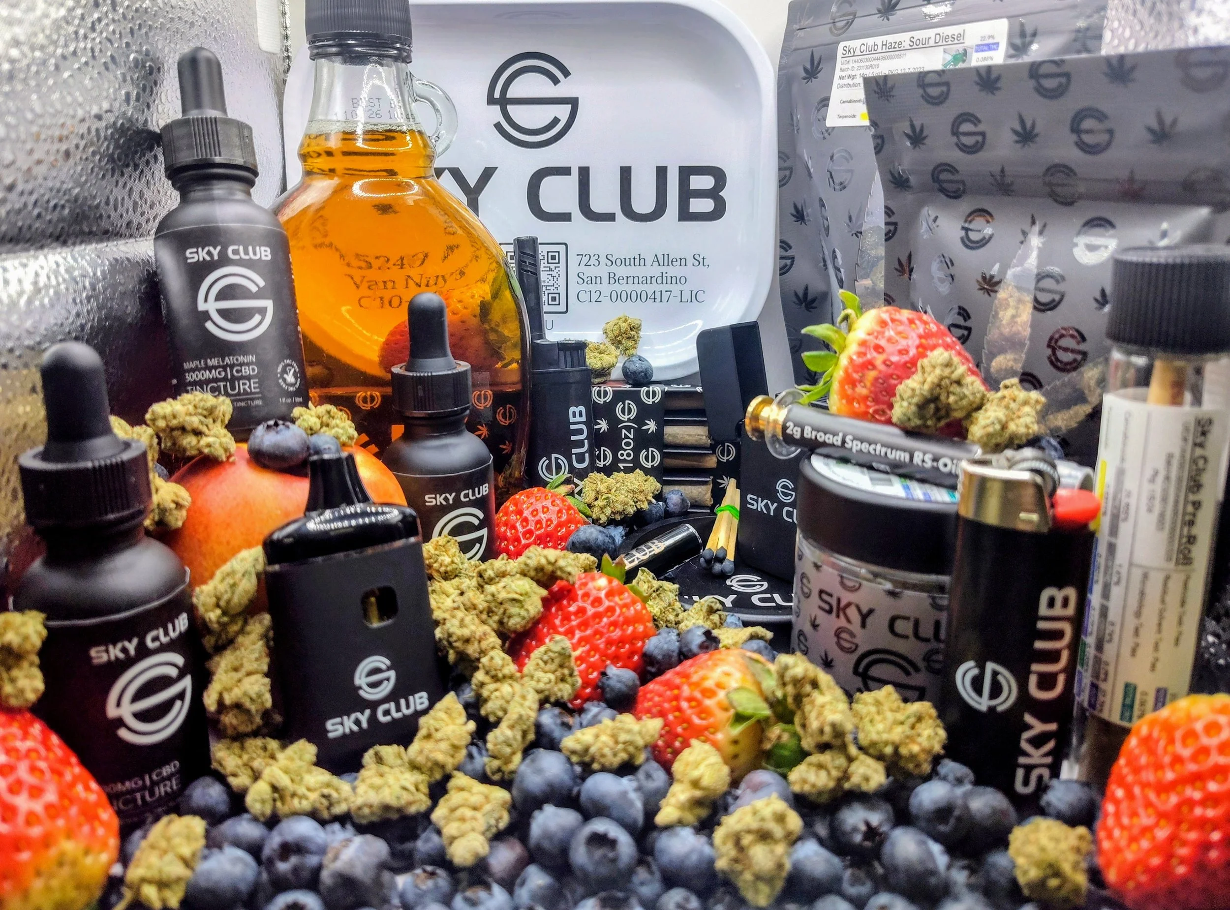 An assortment of cannabis-related products including bottles, cartridges, and jars branded with 'Sky Club,' surrounded by fresh strawberries, blueberries, and cannabis buds.