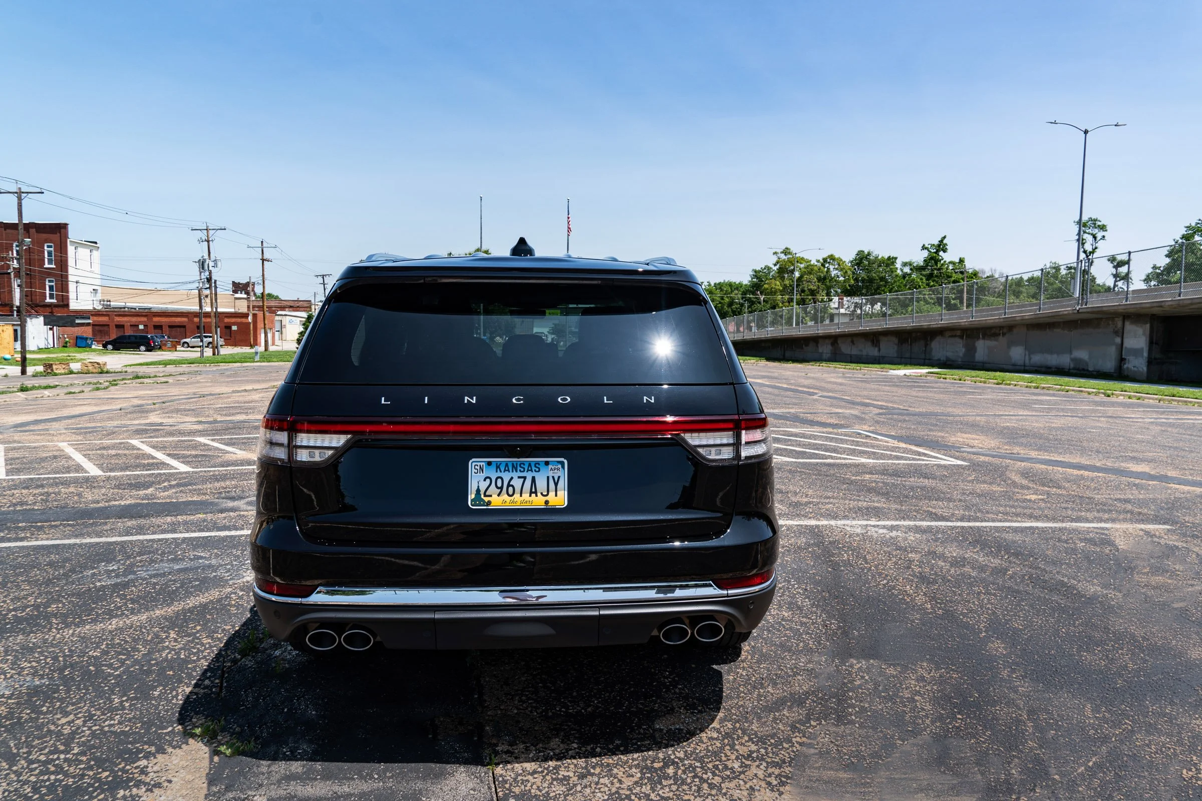A black Lincoln SUV parked in an empty parking lot on a sunny day, with a Kansas license plate and a cityscape in the background.