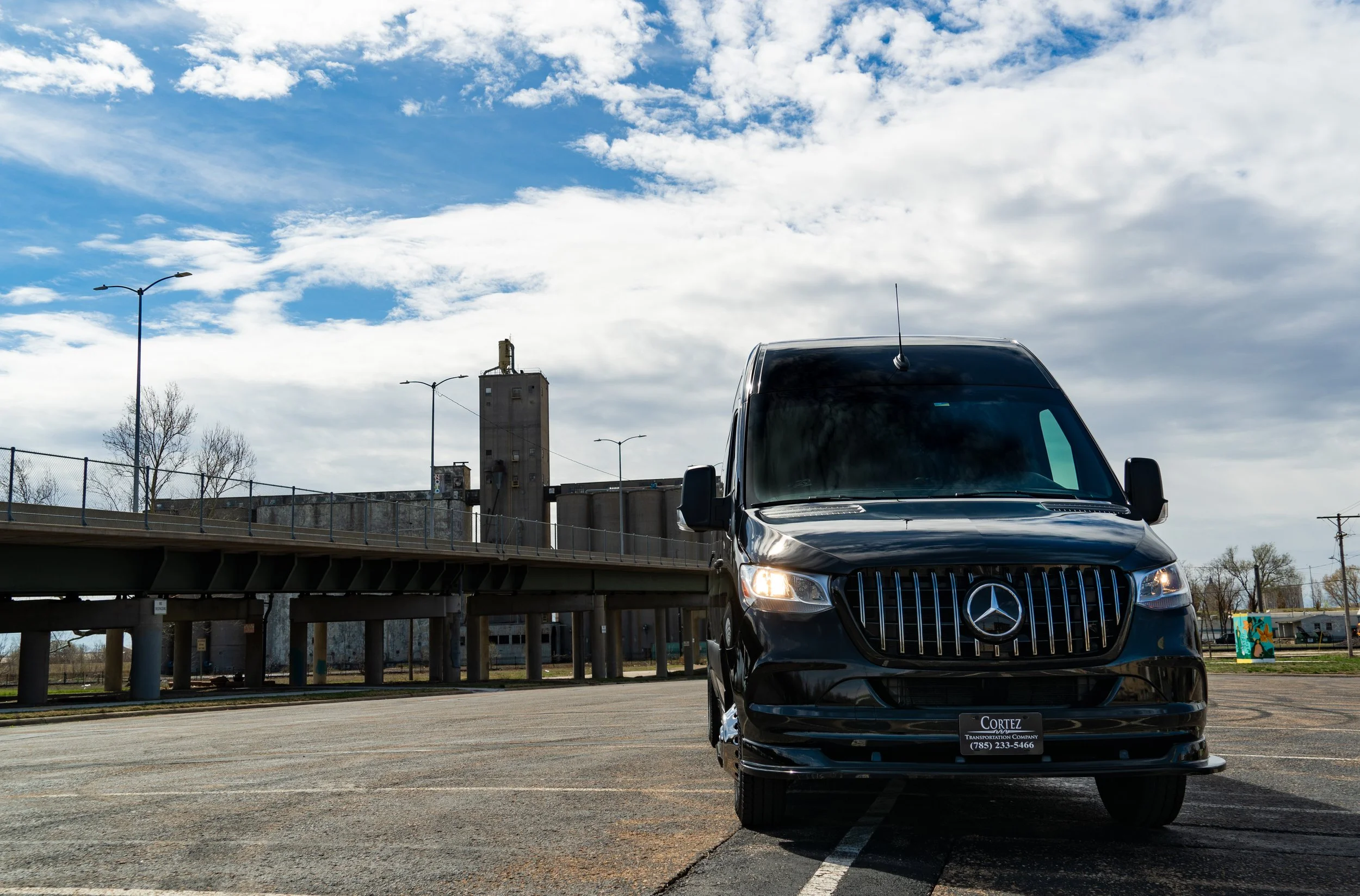 Black Mercedes-Benz van parked in an empty parking lot under a partly cloudy sky.