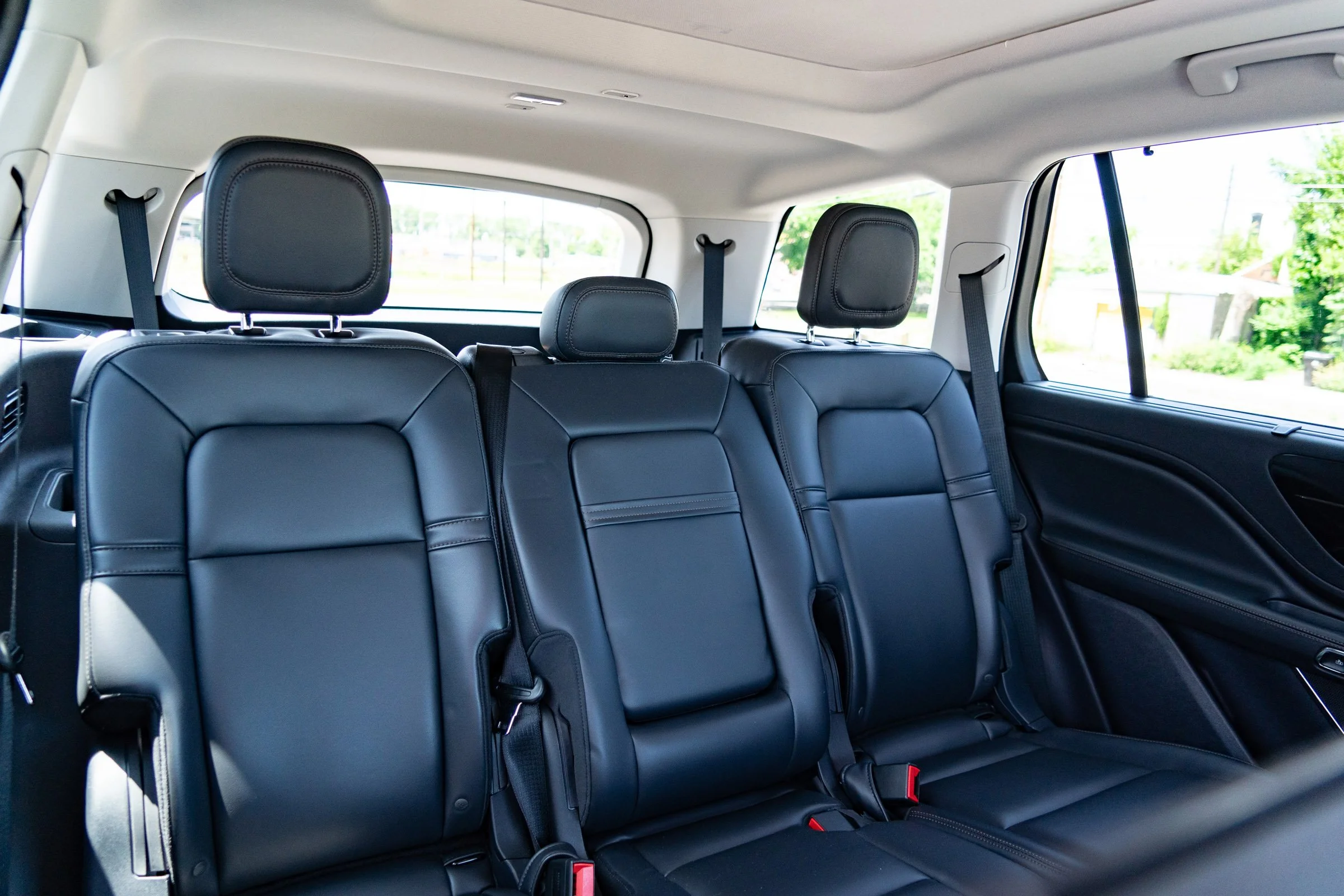 Interior of a vehicle showing three black leather back seats with headrests and seat belts, outside view through windows