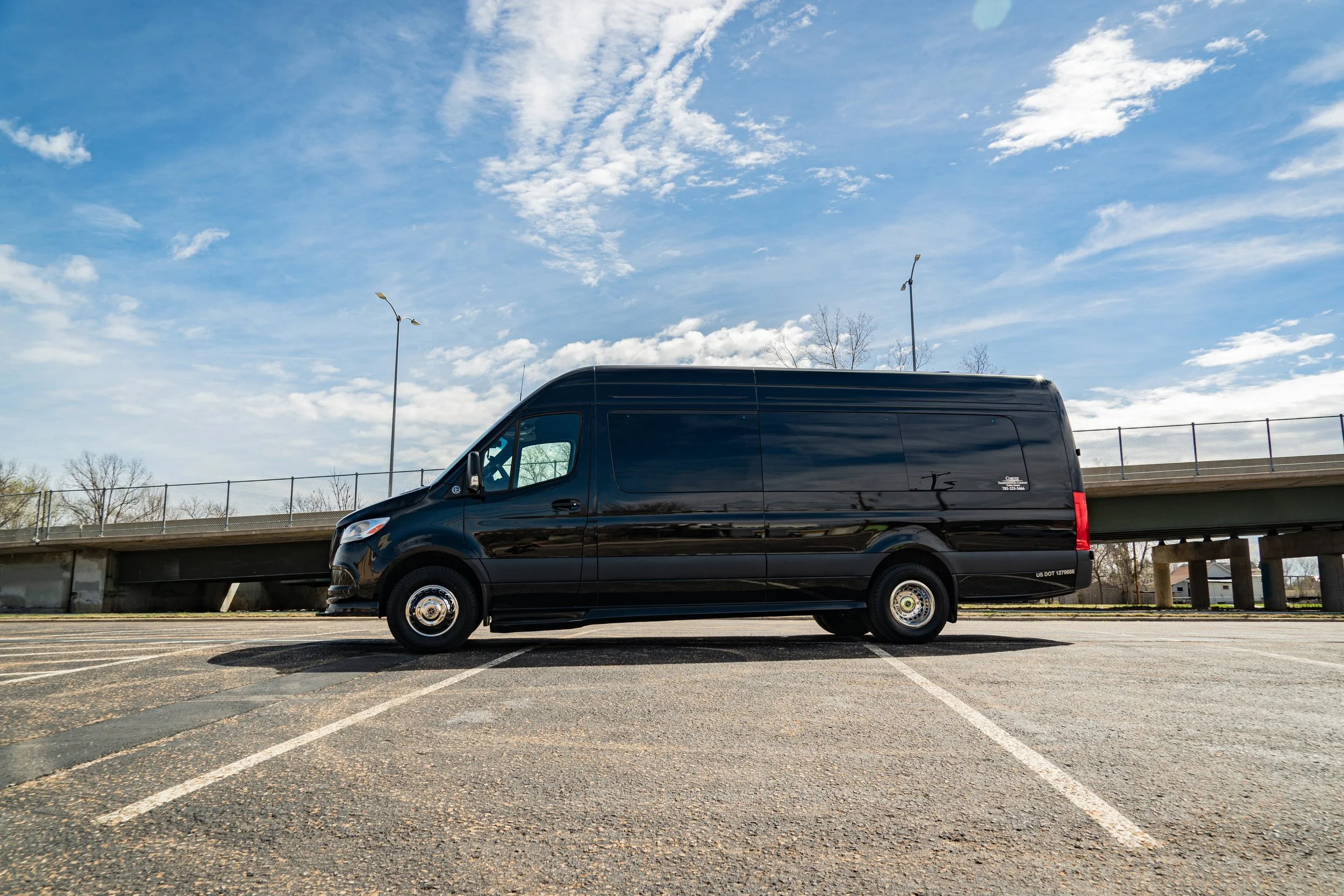 A black cargo van parked in an empty parking lot under a partly cloudy sky.