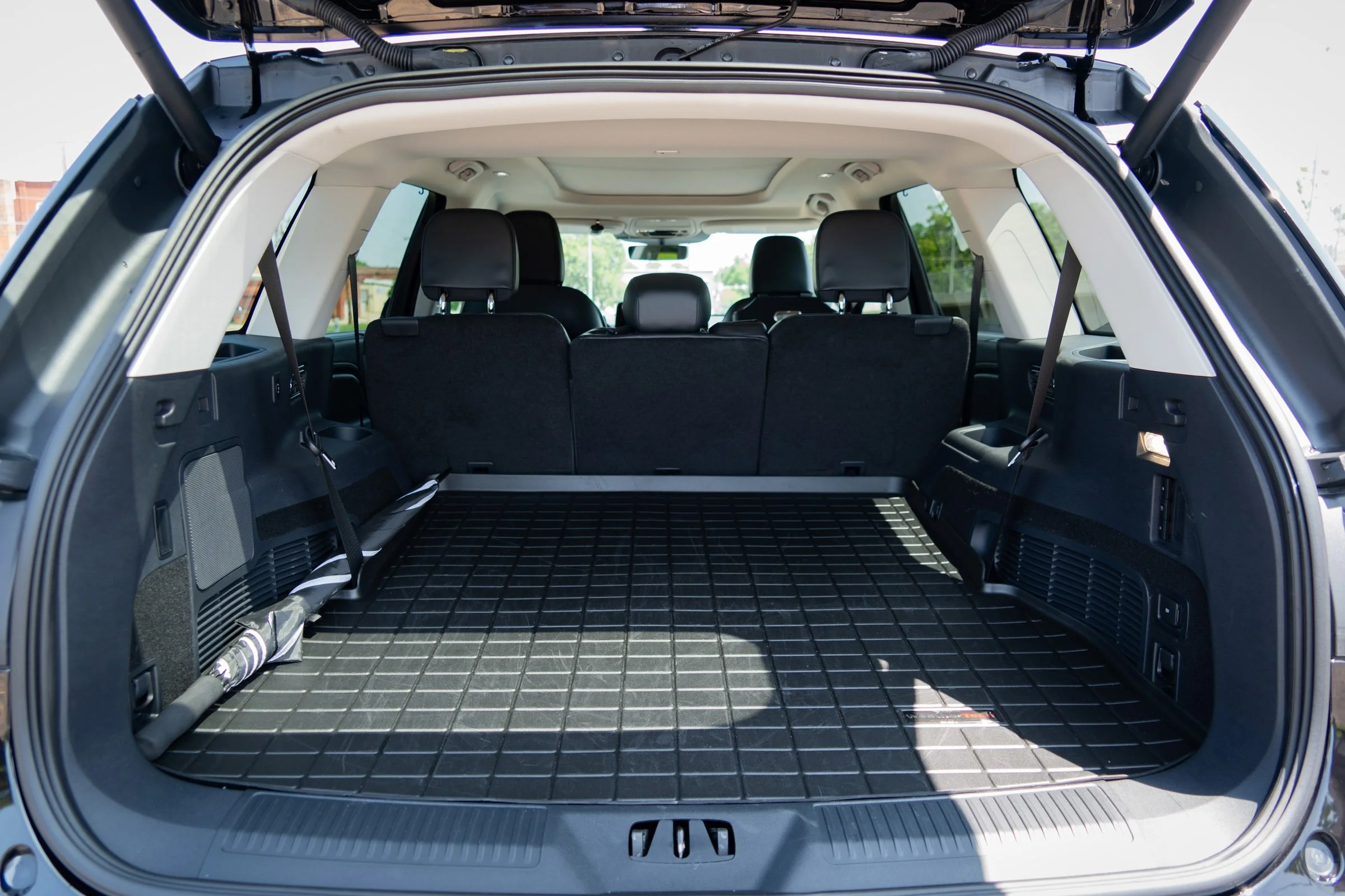 The open trunk of a black SUV showing a spacious cargo area with a grid-patterned rubber mat on the floor and three black rear seats upright.
