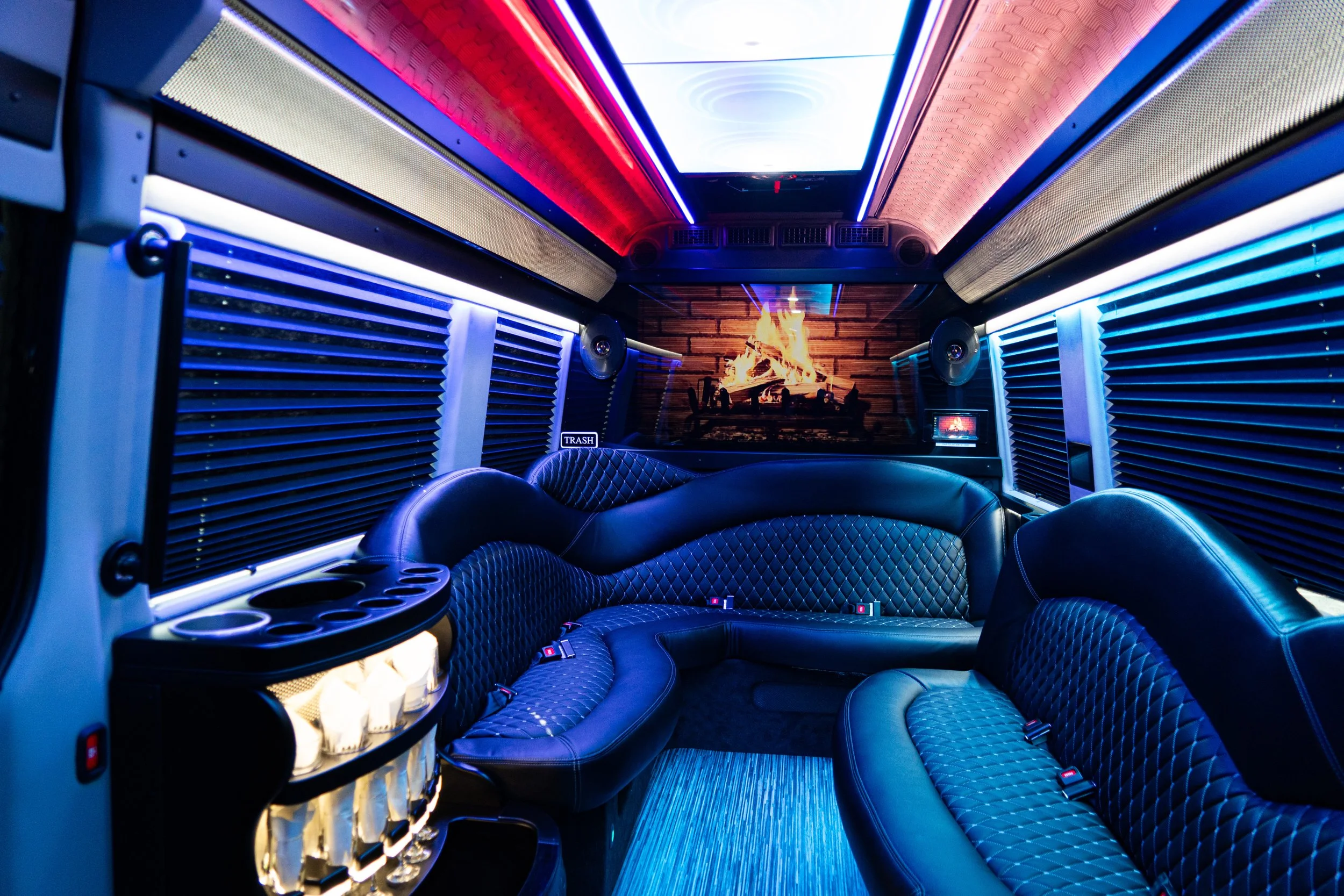 Luxurious limousine interior with black leather diamond-stitched seating, a fireplace, LED lighting, and a built-in liquor cabinet.