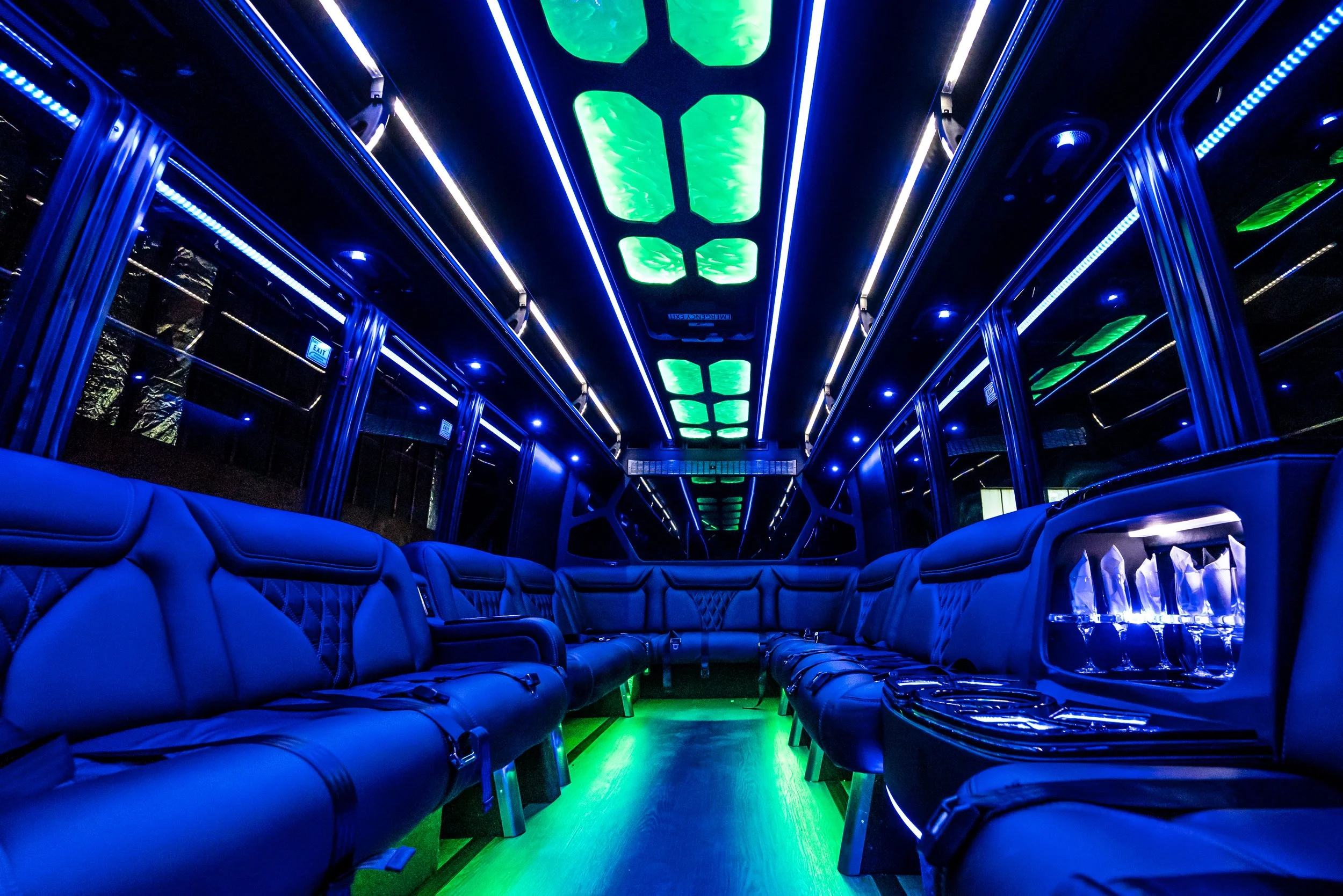 Interior of a luxury bus with black leather seats and vibrant neon green and blue lighting along the ceiling and floor.