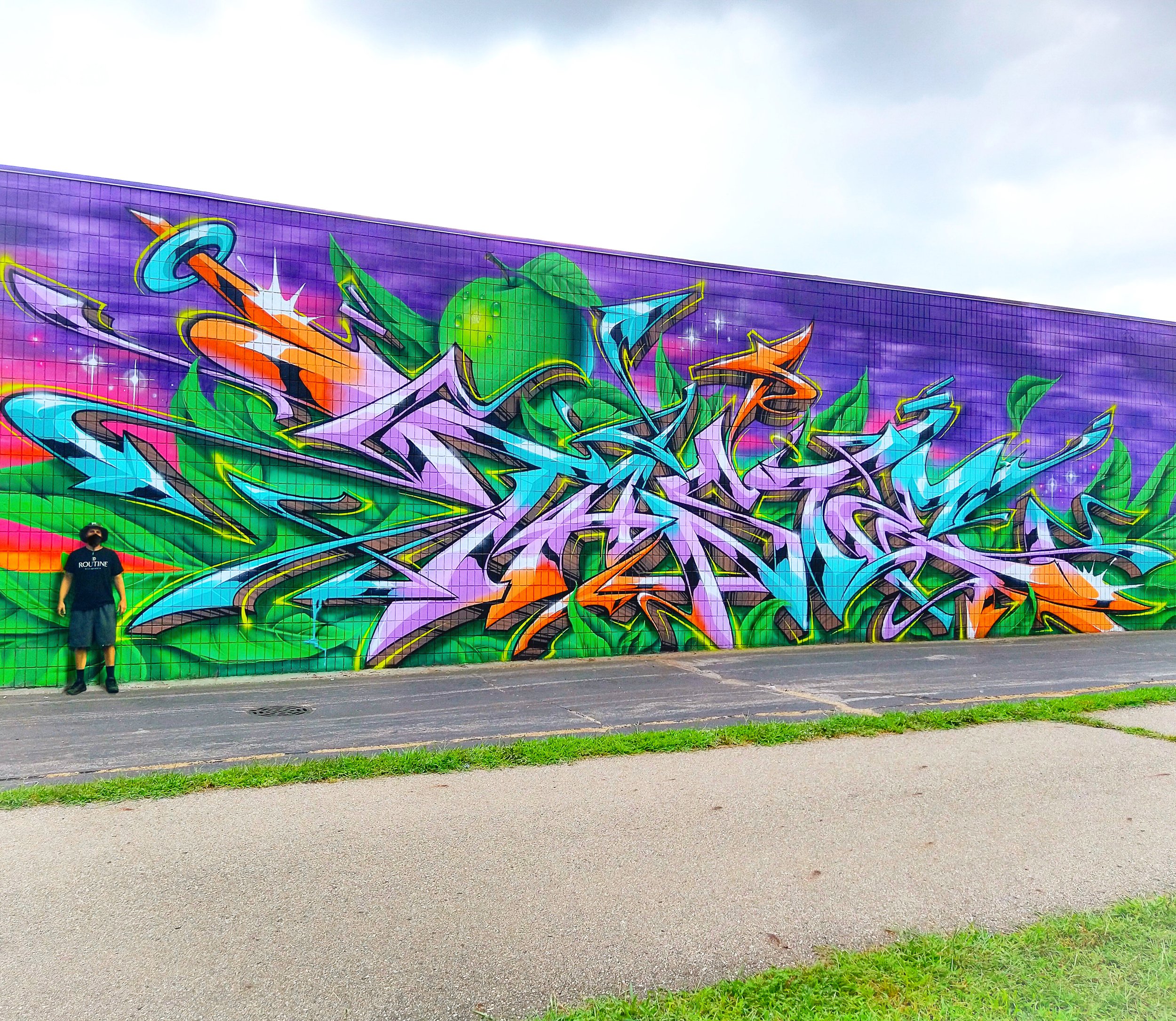 large vibrant nature inspired graffiti mural on massive tile wall featuring the artist standing in front of his work for scale