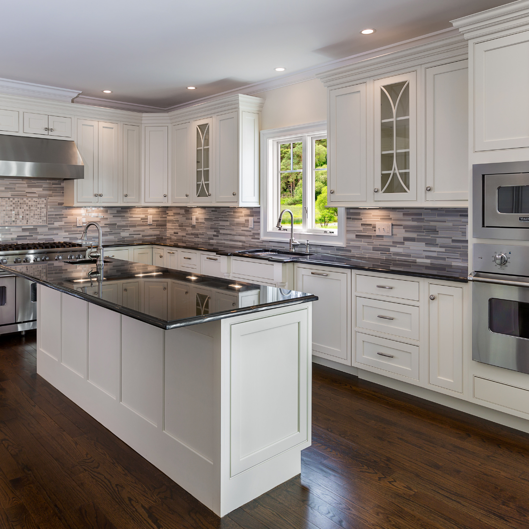 Modern kitchen with white cabinets, black countertop island, gray mosaic tile backsplash, stainless steel appliances, and a window with a view of green trees.