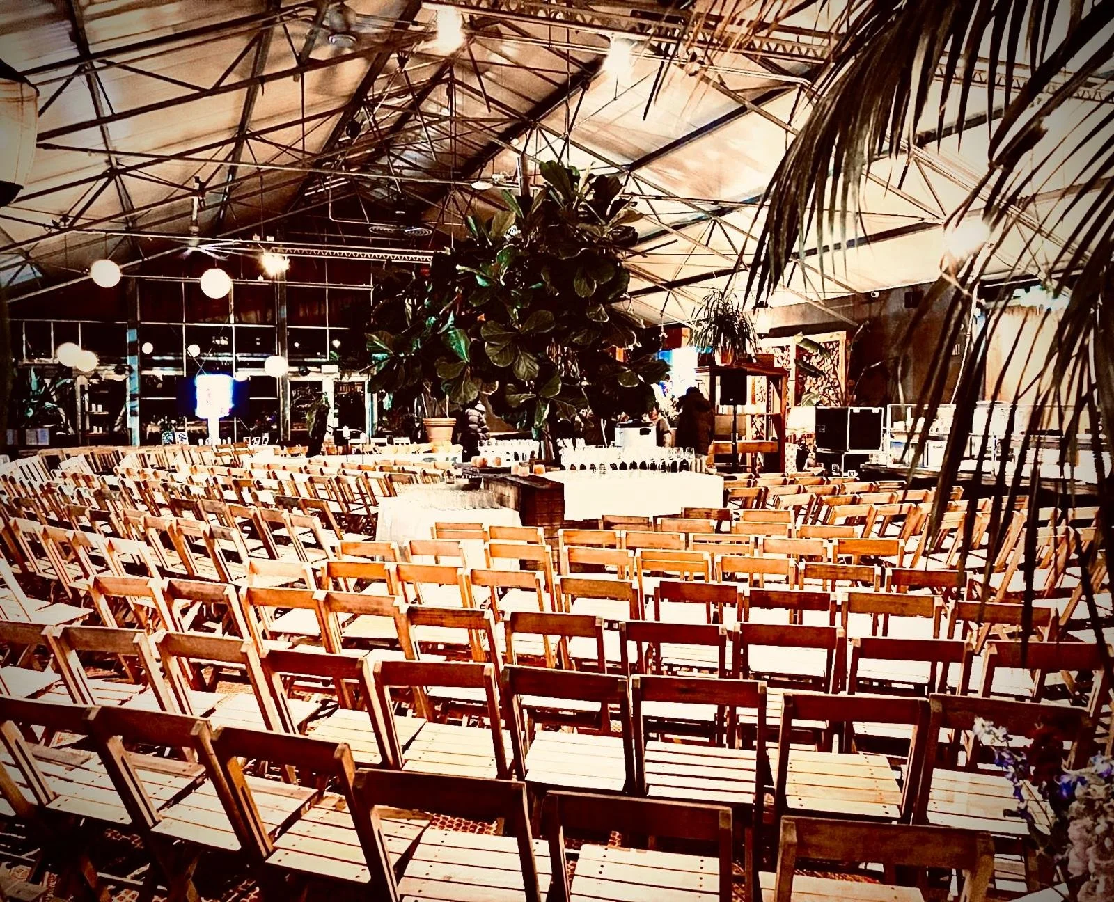 Industriële feestzaal met houten stoelen en groene planten, klaar voor een evenement.