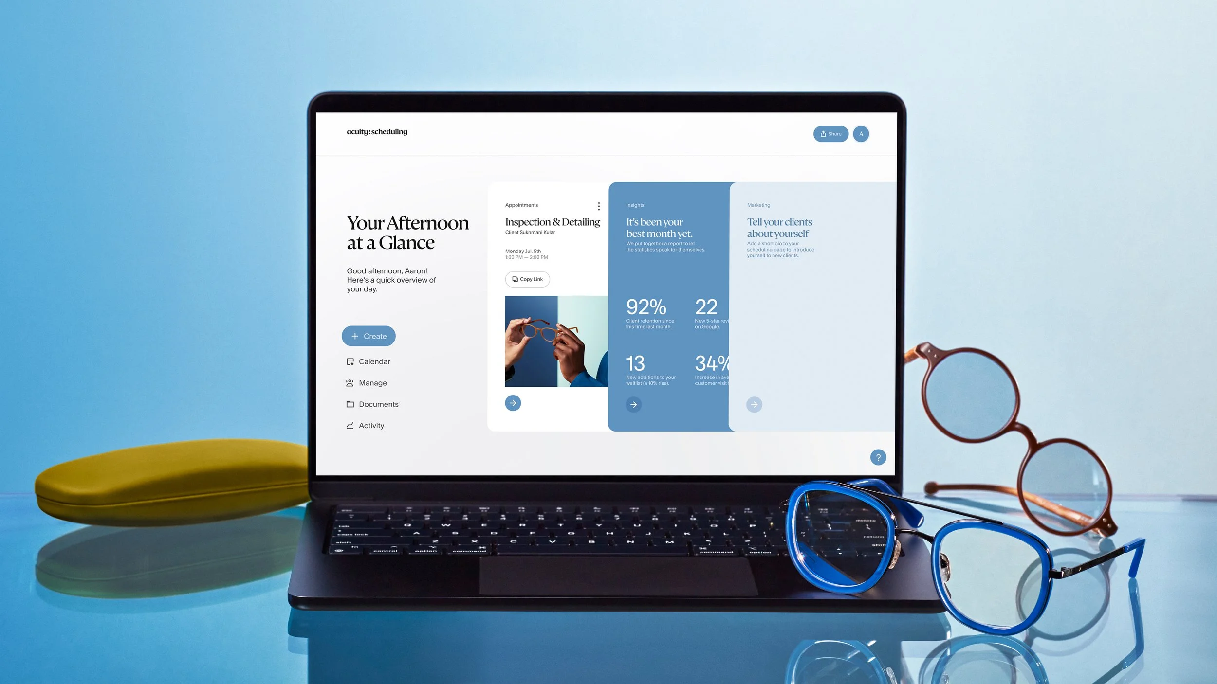 A laptop showing a scheduling and analytics app on a blue surface, accompanied by two pairs of glasses, a yellow glasses case, and a blue glasses frame.