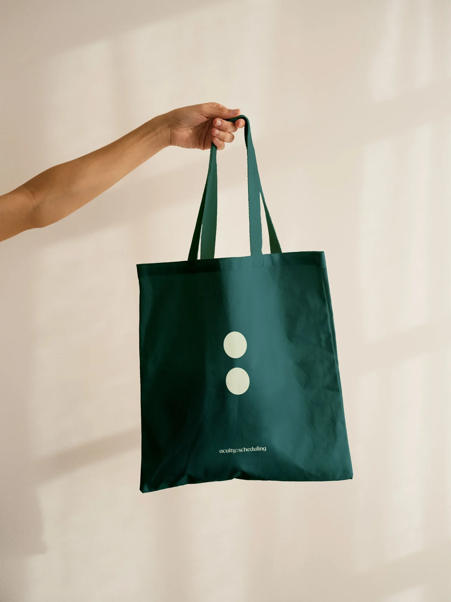 Hand holding a green tote bag with two white circles and small white text.